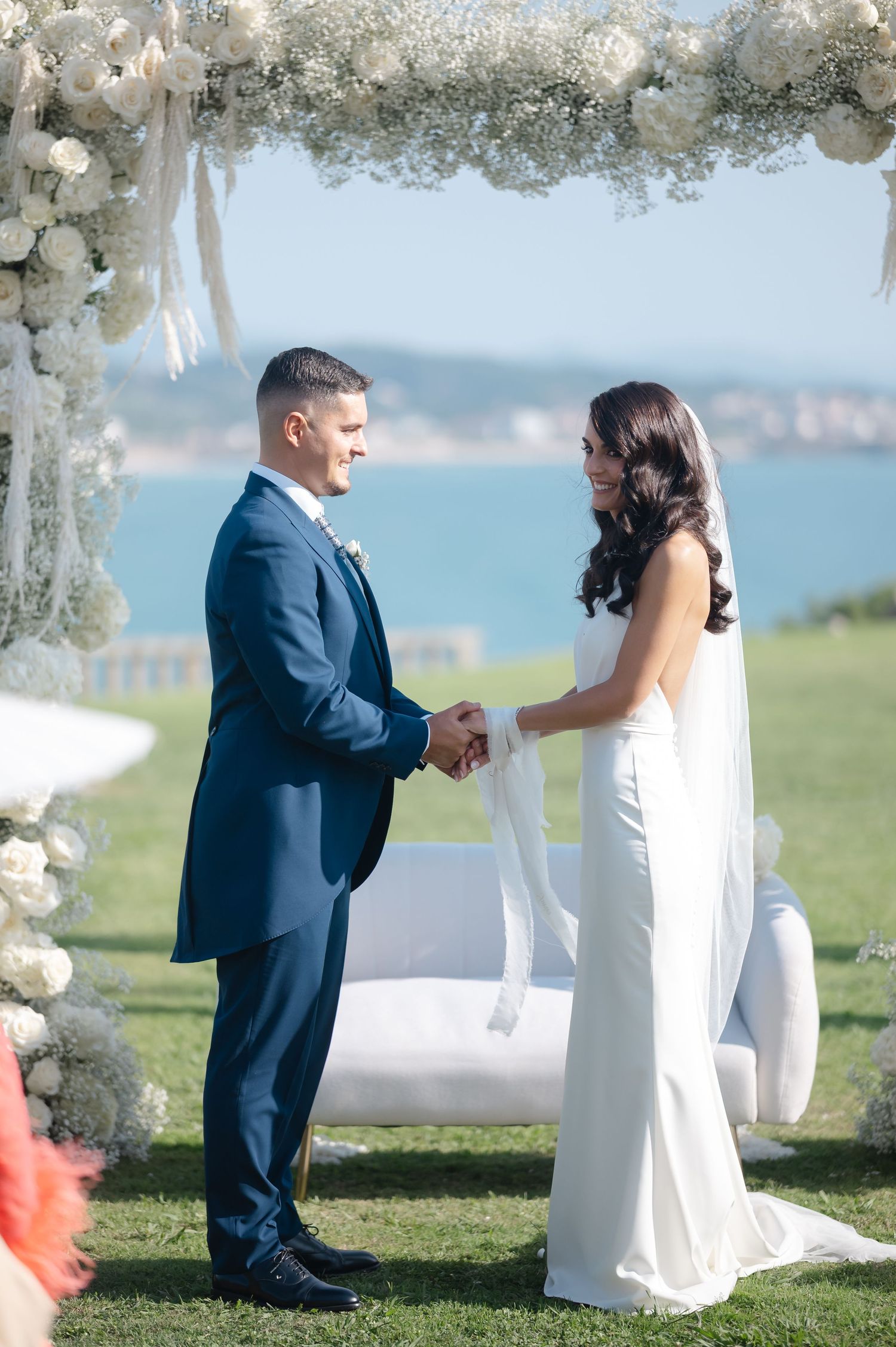 Wedding ceremony setup with white floral arch and seating arrangements against a beautiful ocean backdrop.