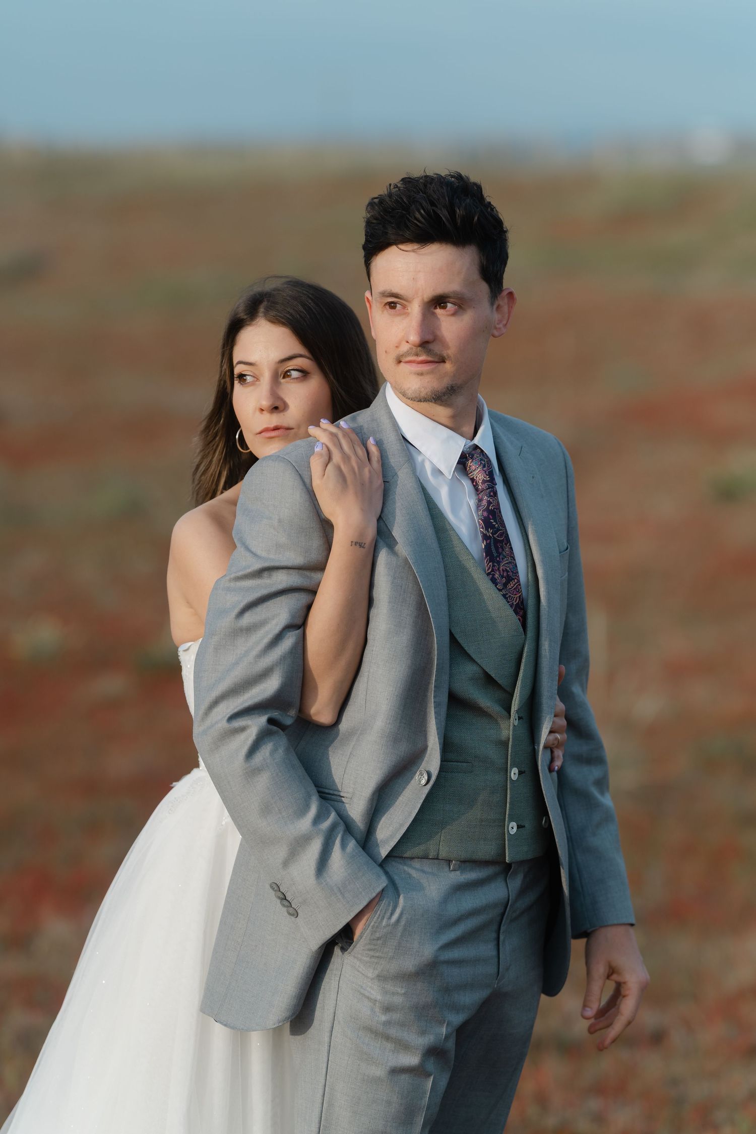 Bride embraces groom from behind in a colorful field during outdoor wedding portrait session.
