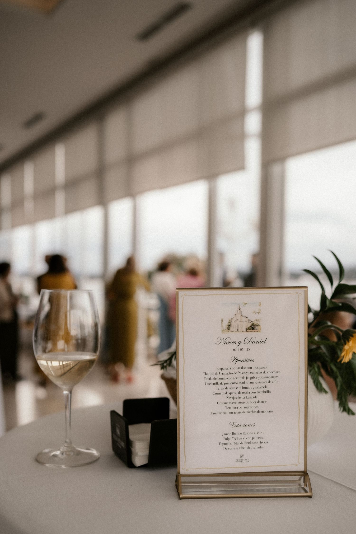 Wine glasses and elegant menu cards are arranged on a white tablecloth at an upscale wedding reception.