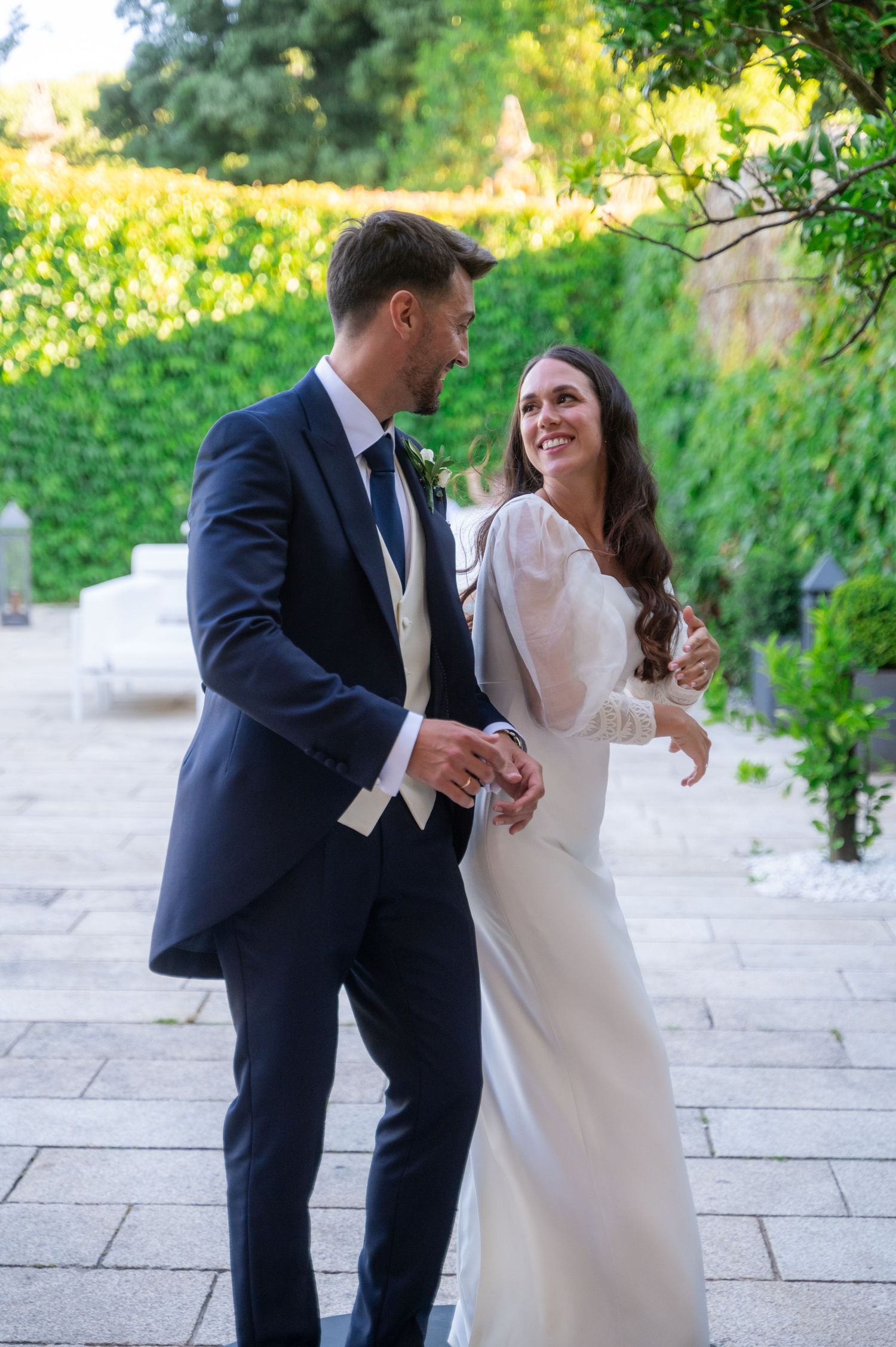 A couple shares a joyful moment together during a wedding photoshoot on a stone patio with greenery in the background.