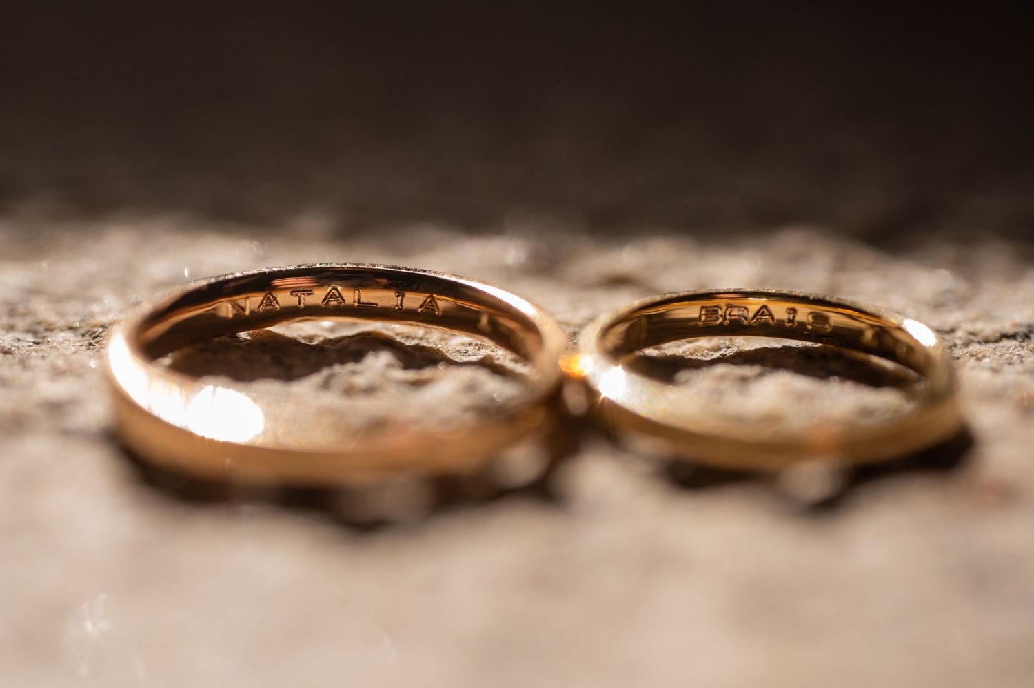Two gold wedding rings photographed in close-up on a textured surface with shallow depth of field.