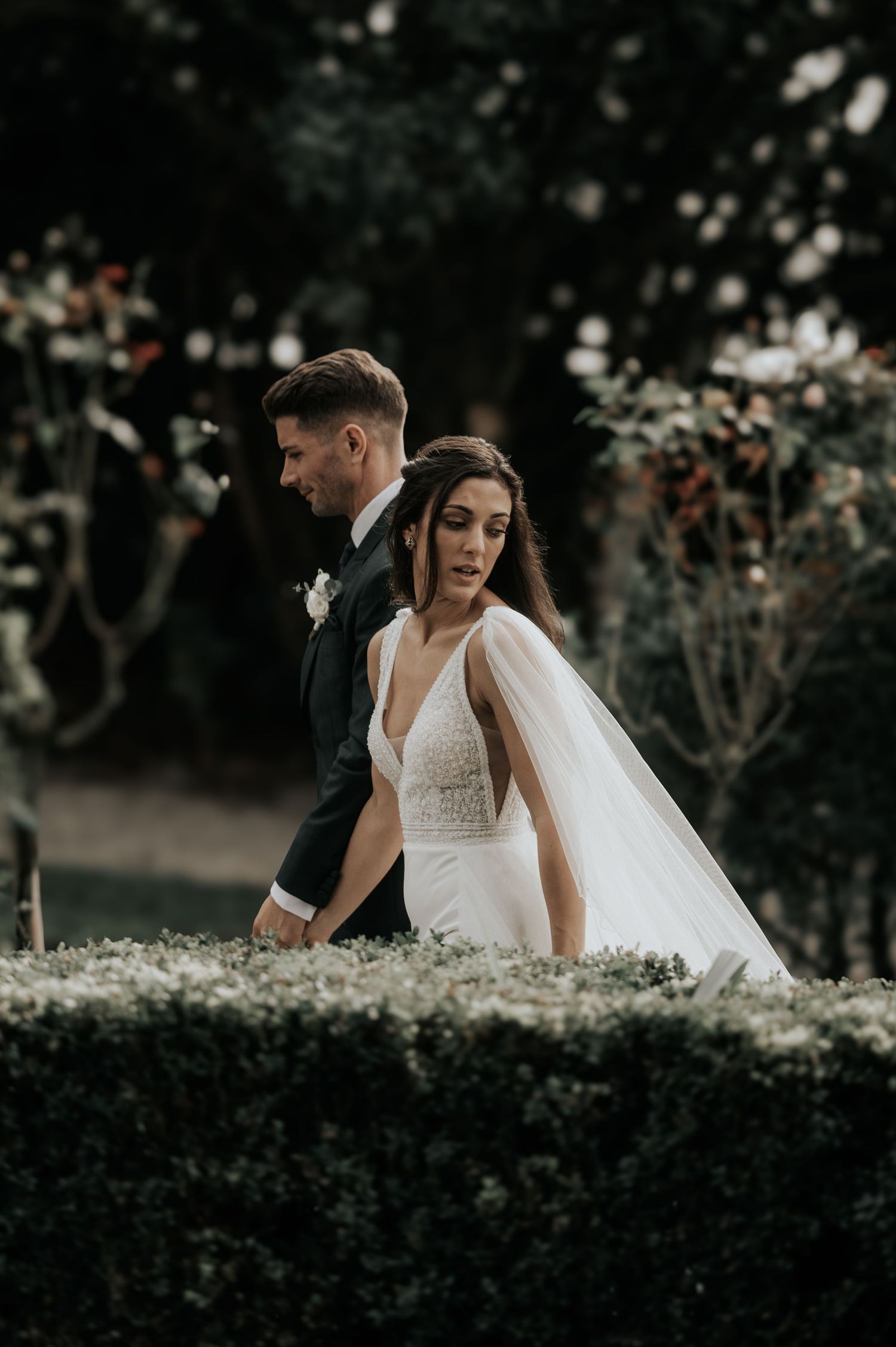 Romantic wedding couple poses among blooming garden flowers at sunset.