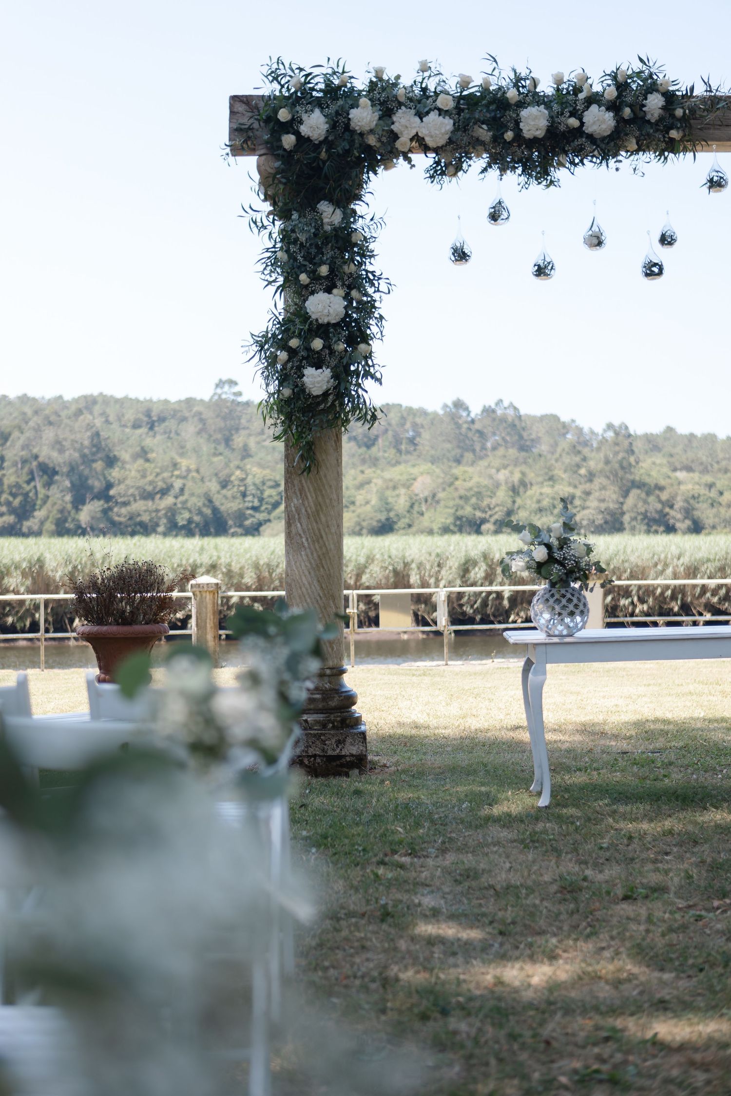 Outdoor wedding venue setup with white columns and floral arches arranged on grassy field.