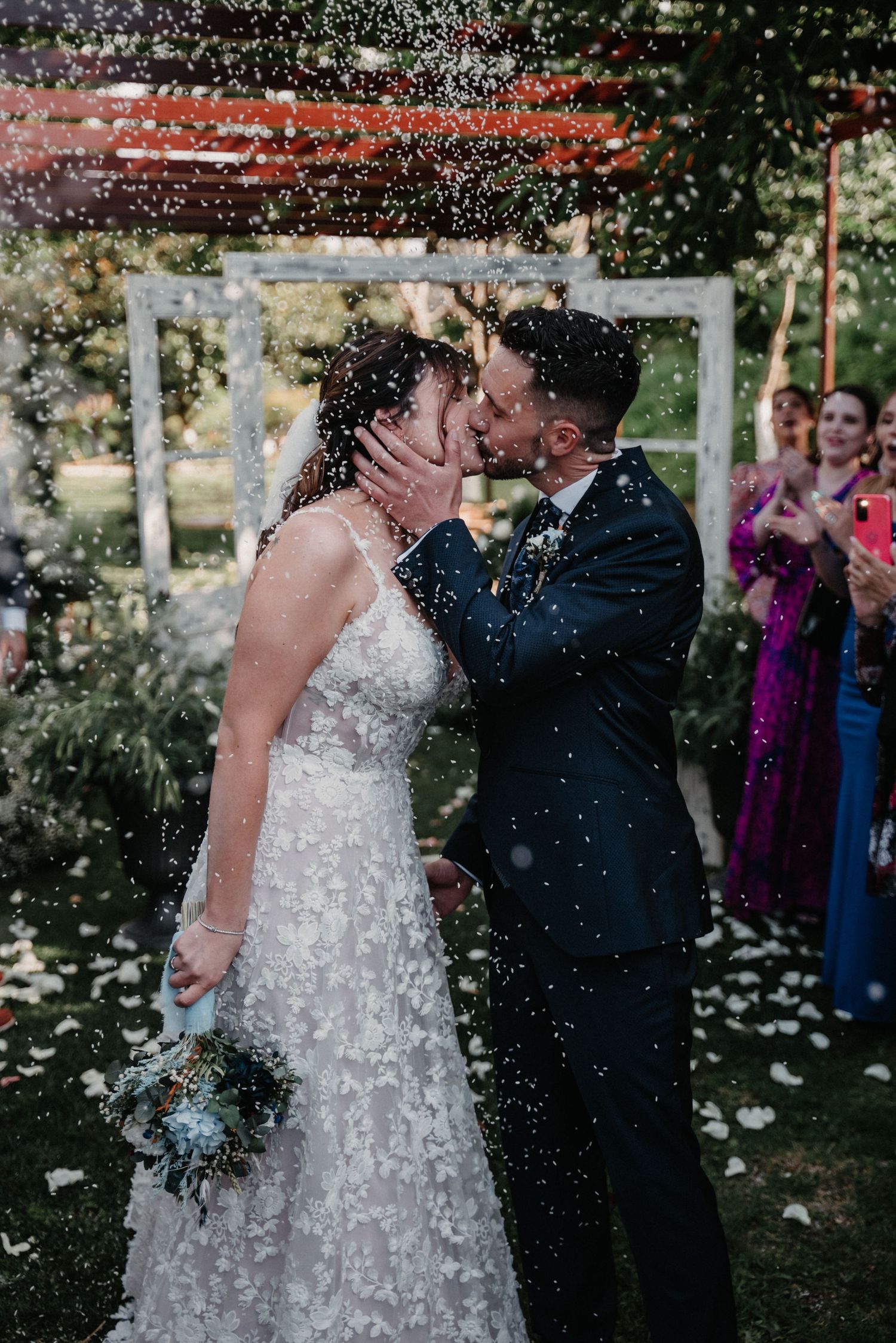Newlyweds celebrate with confetti shower at outdoor garden wedding ceremony.
