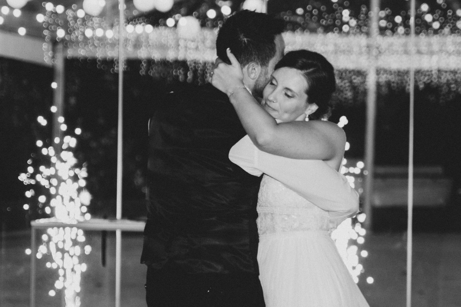 A bride and groom share their first dance at a wedding reception with sparklers glowing in the background.
