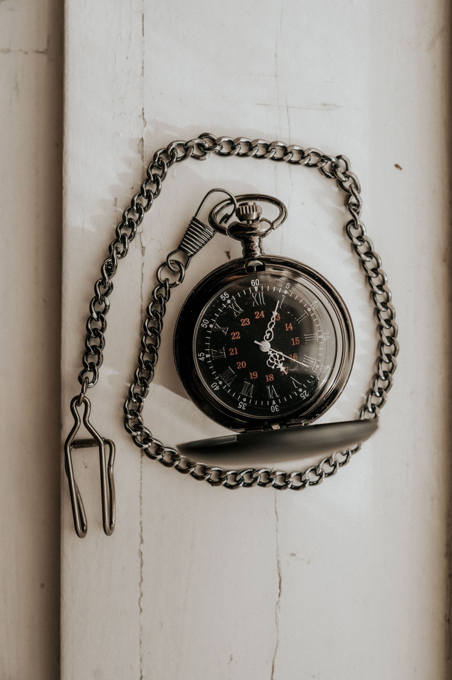 Vintage black pocket watch with chain lying on white wooden surface in moody lighting.