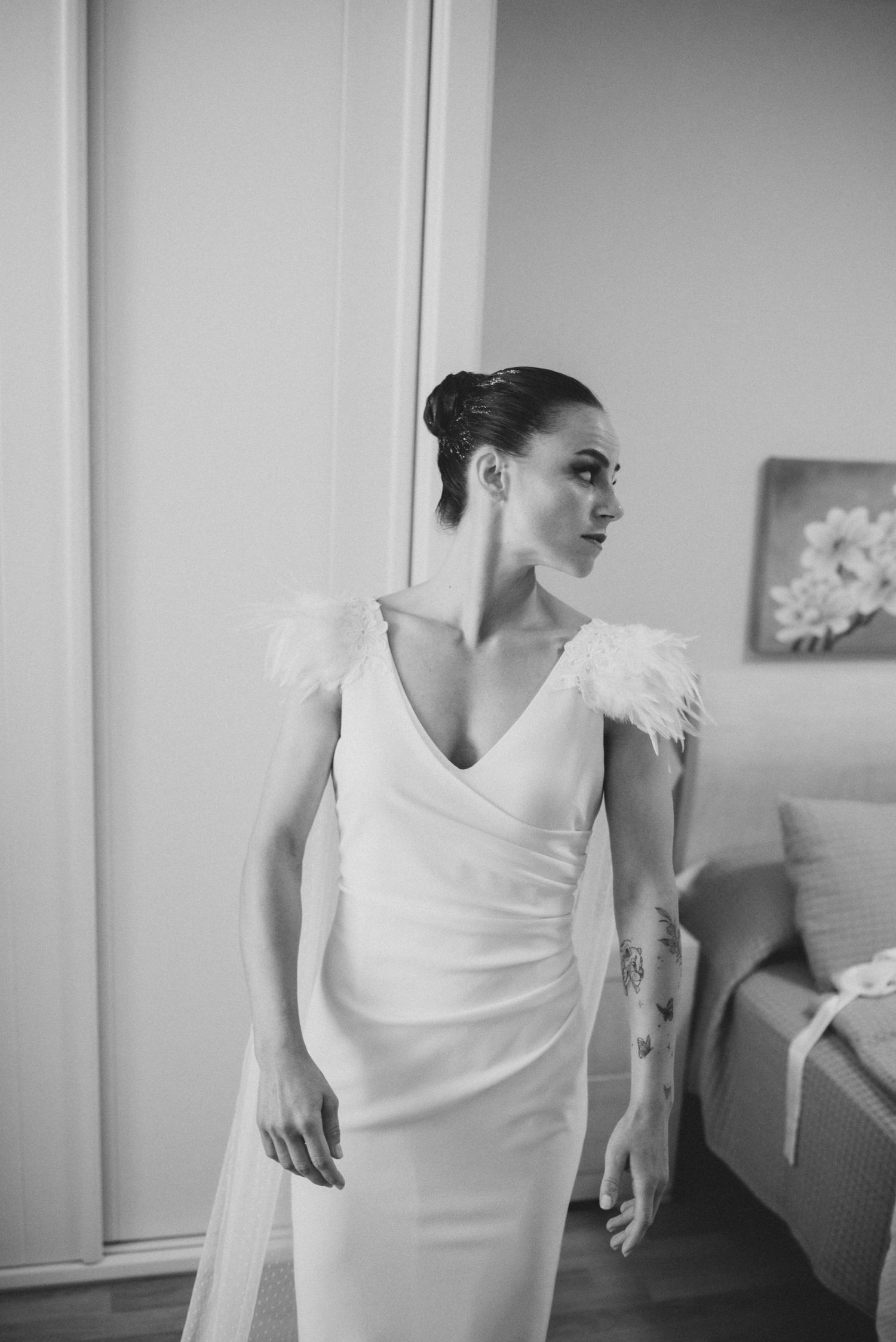 Elegant white wedding dress with feathered cap sleeves and fitted silhouette shown in black and white photograph.