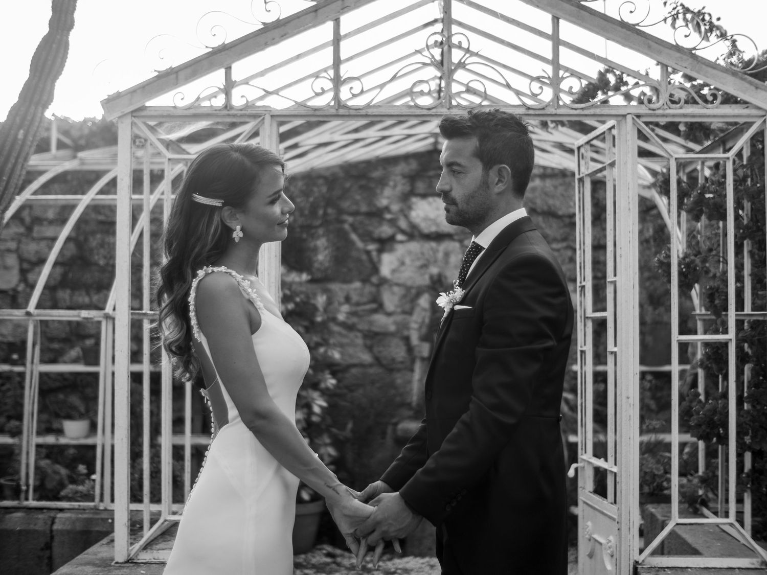 A couple shares a tender moment during their wedding ceremony in a glass-enclosed greenhouse venue.