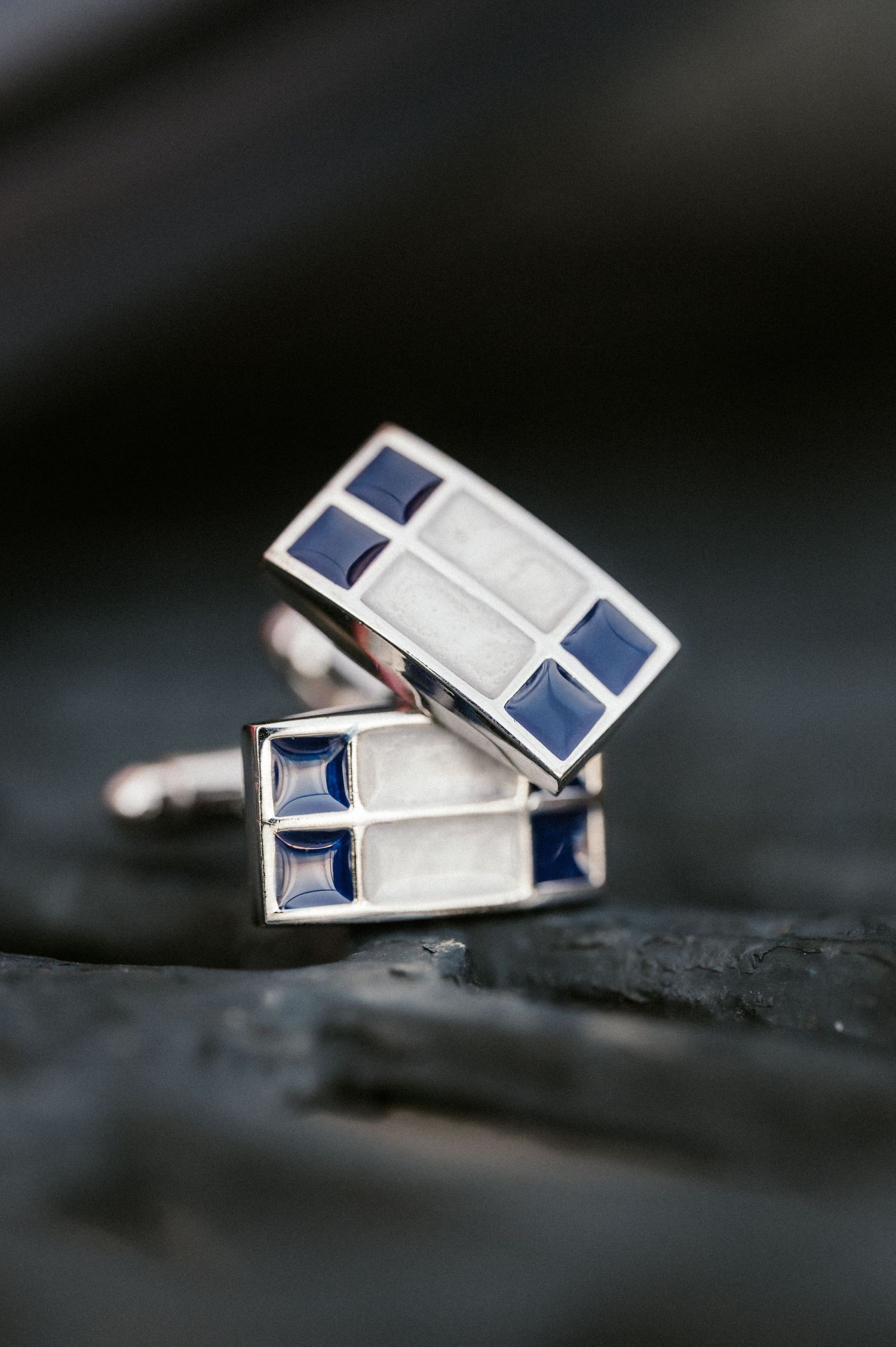 Silver cufflinks with blue sapphire stones shown in multiple angles on a dark textured surface.