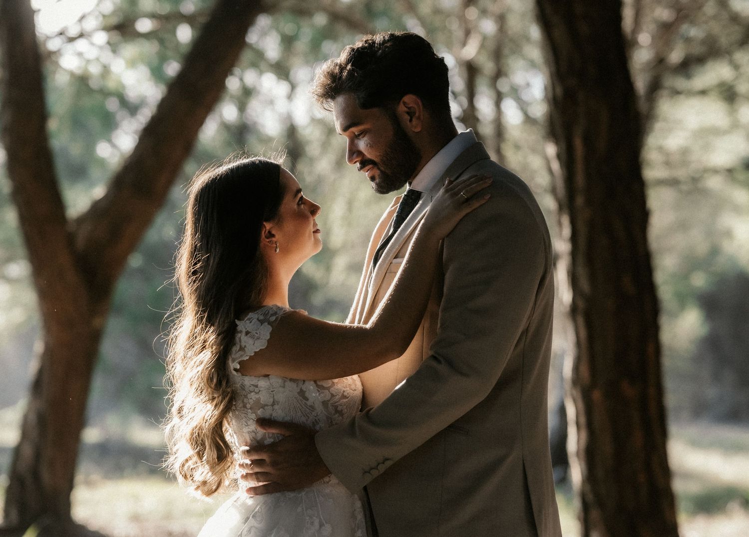 A romantic couple embraces in a dreamy forest setting with soft sunlight filtering through the trees.