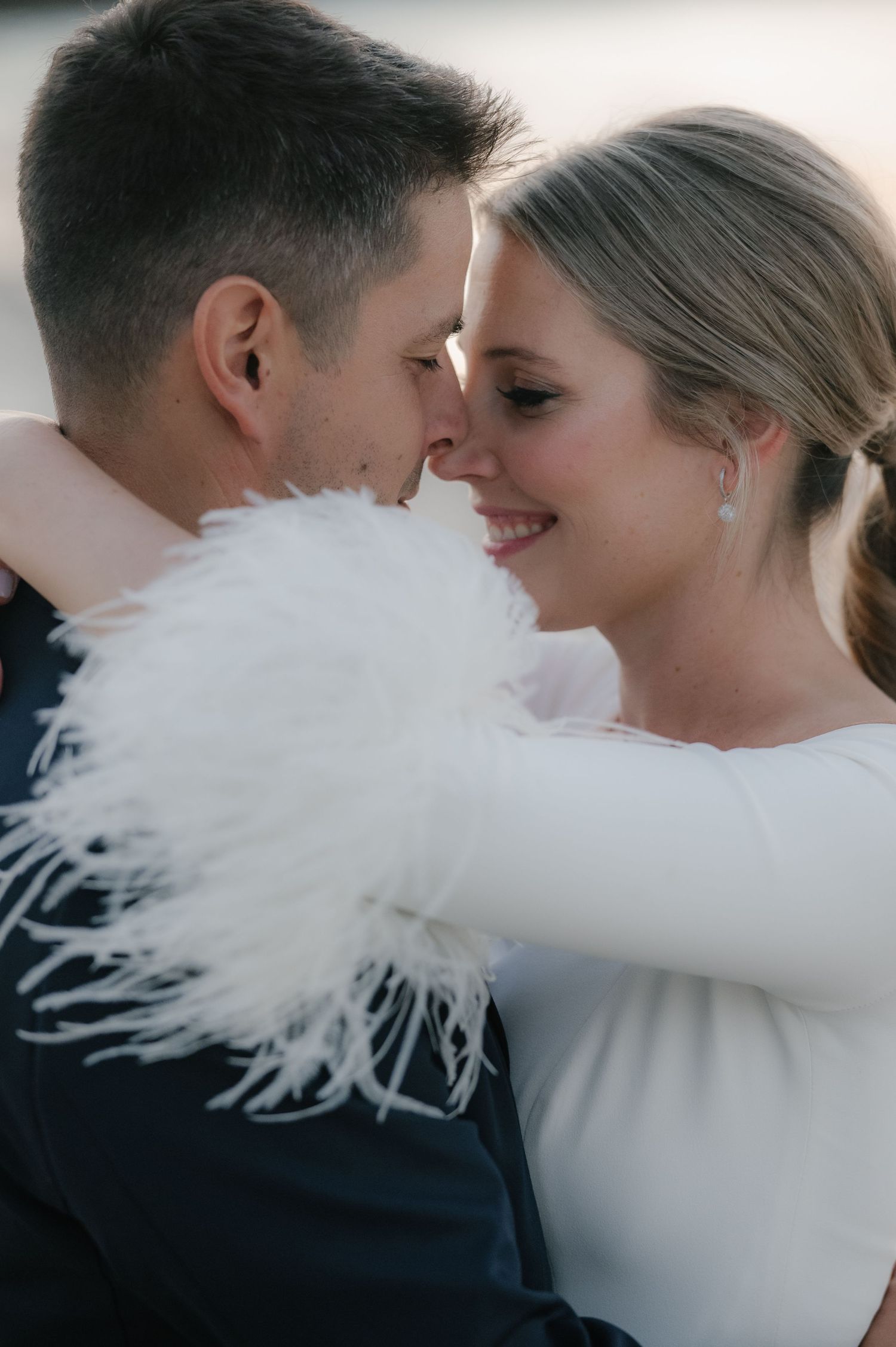 Close-up wedding portrait showing white feathered sleeve detail against soft background.