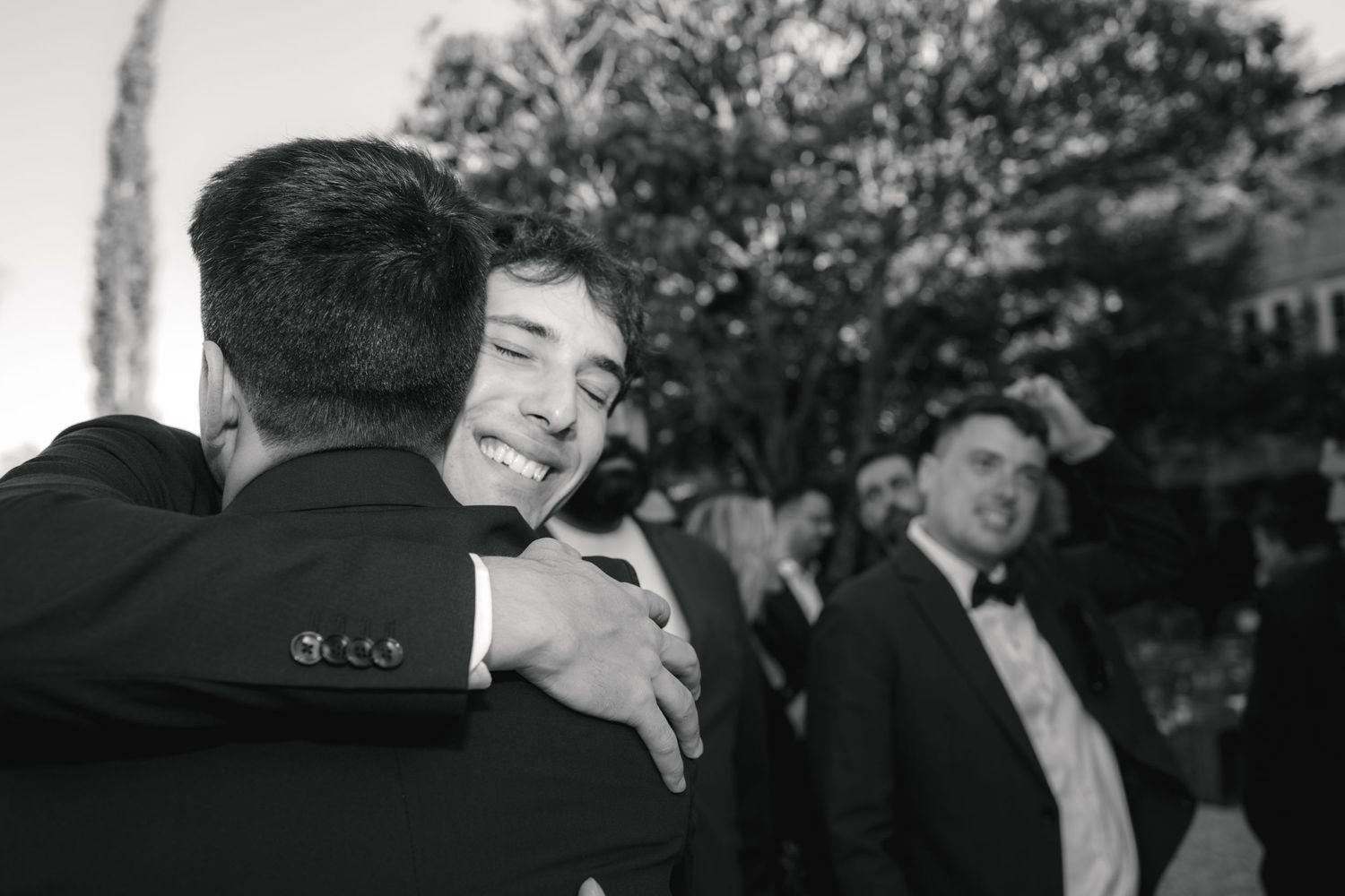 Emotional black and white photograph of wedding guests embracing during celebration.