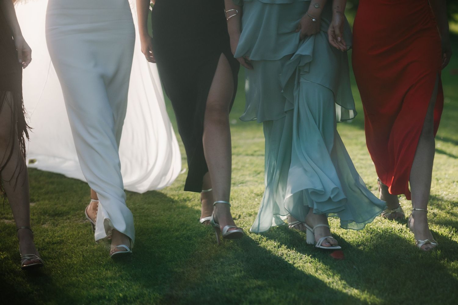 Wedding party members in formal attire standing on grass in natural sunlight.