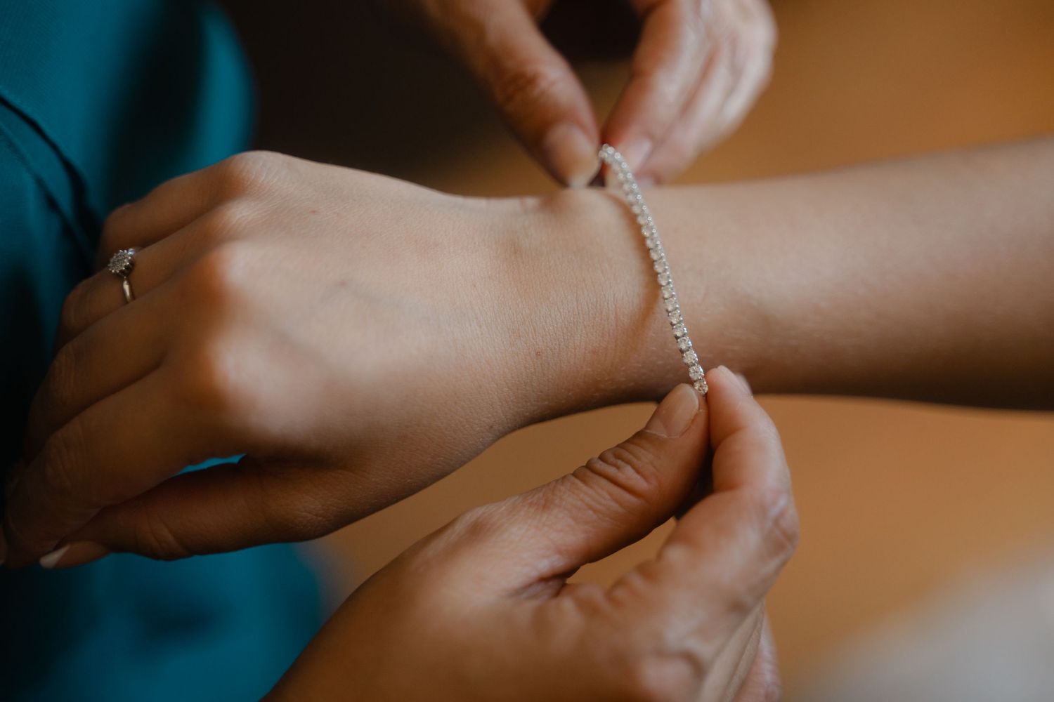 Close-up shot of a diamond bracelet being fastened around a wrist in warm lighting.