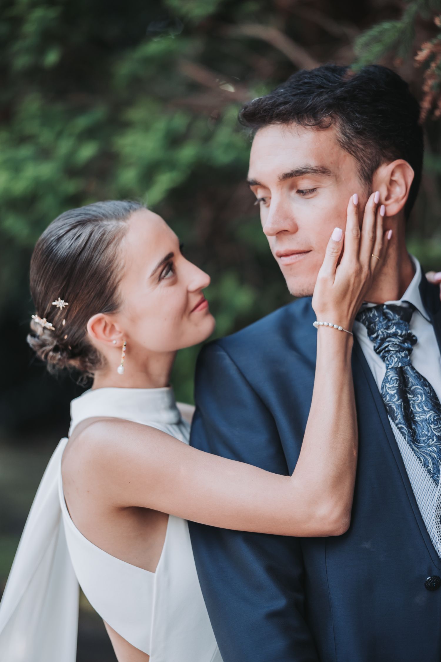 A tender moment between newlyweds as they embrace against a lush green outdoor backdrop.