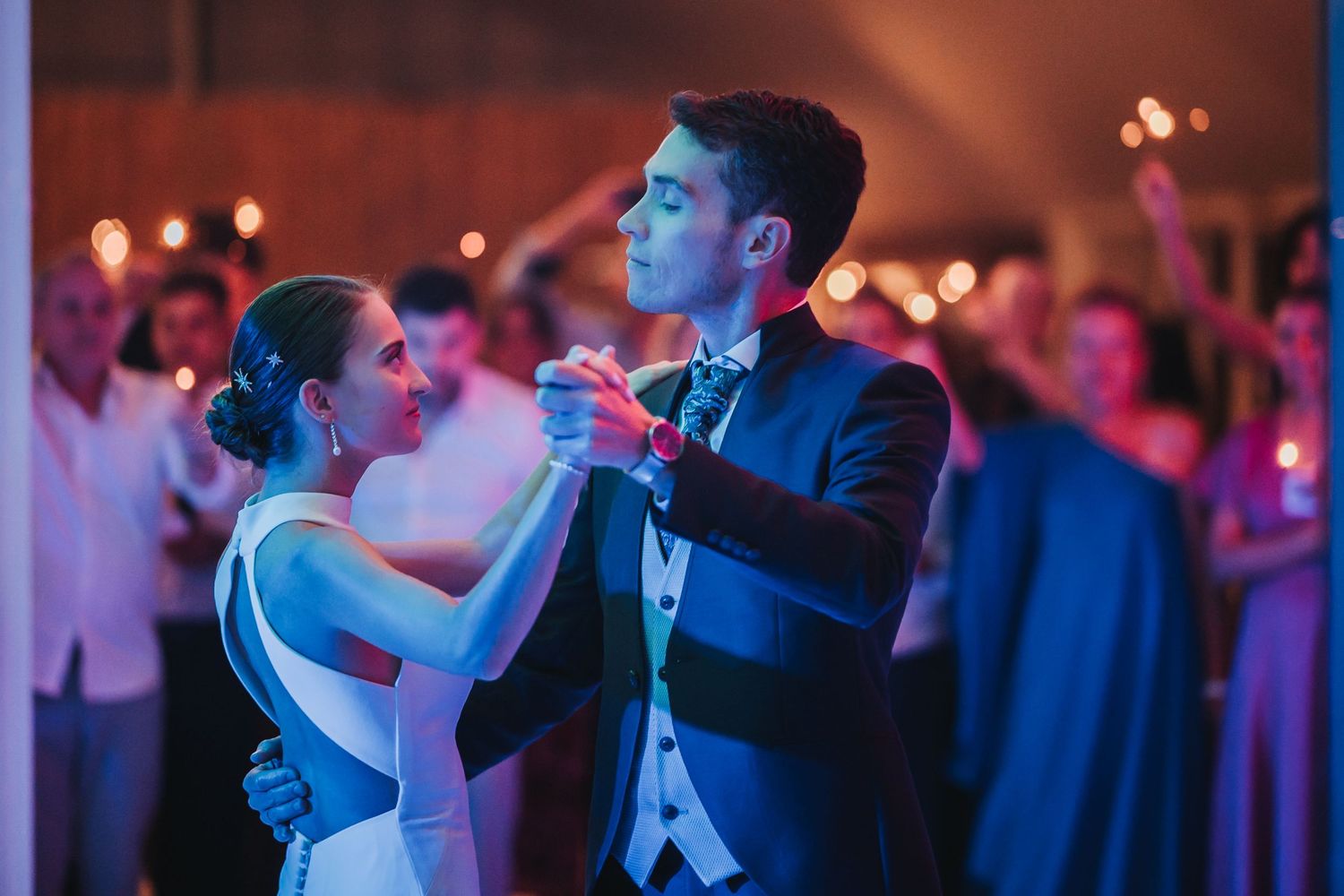 A couple shares their first dance at a wedding reception with purple mood lighting illuminating the romantic moment.