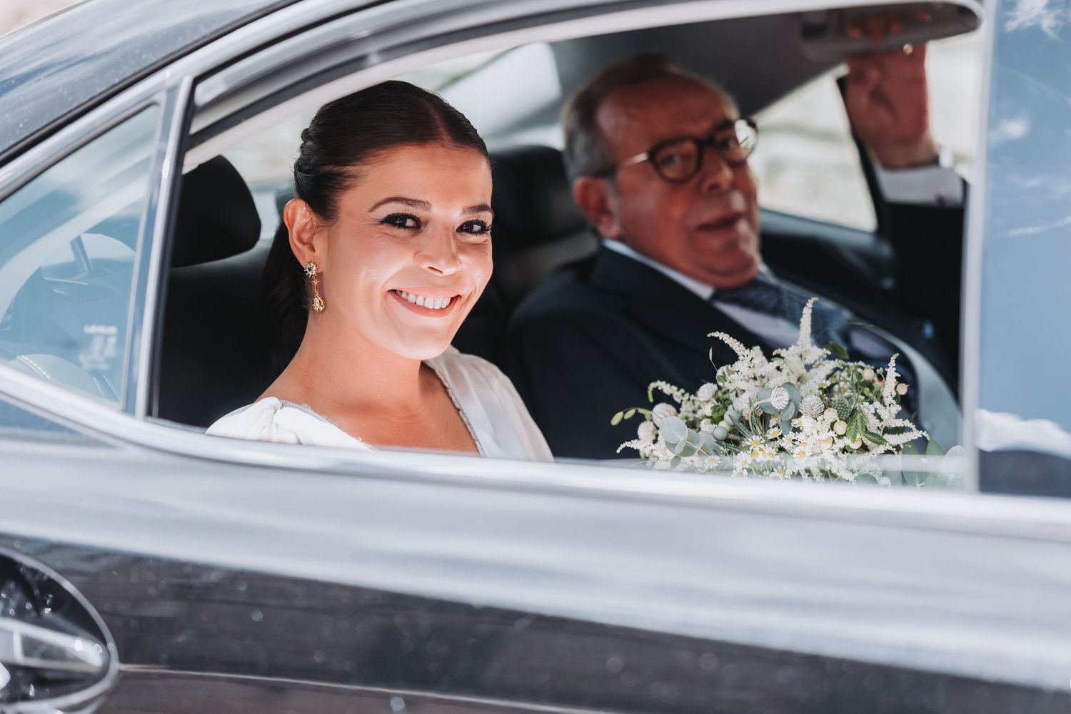 A wedding day scene showing a car interior with a delicate white bouquet of flowers.