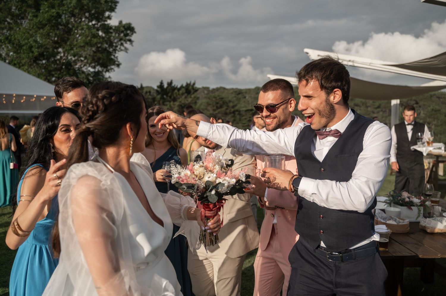 Wedding celebration with guests dancing and mingling under cloudy skies at outdoor venue.