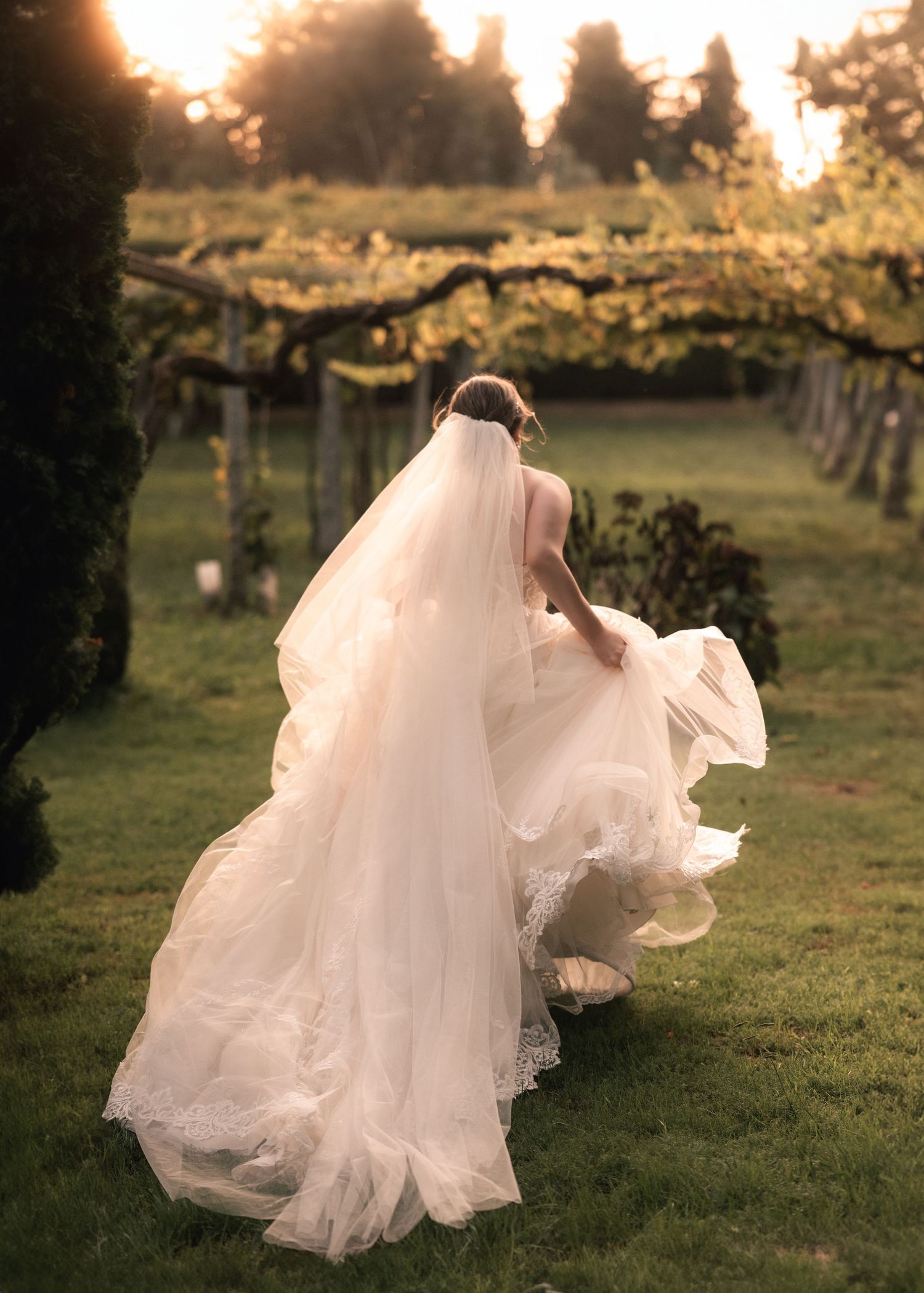 Flowing white wedding dress train spreads across green grass at sunset.