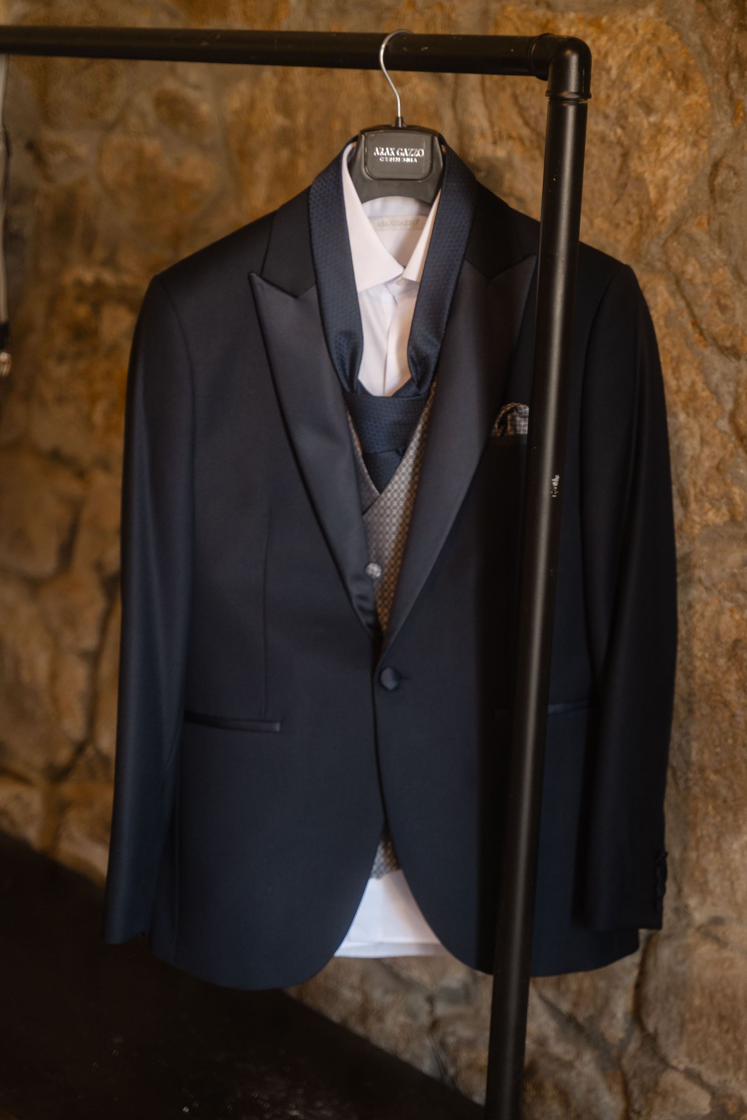 Black formal suit jackets hanging on clothing rack against rustic stone wall.