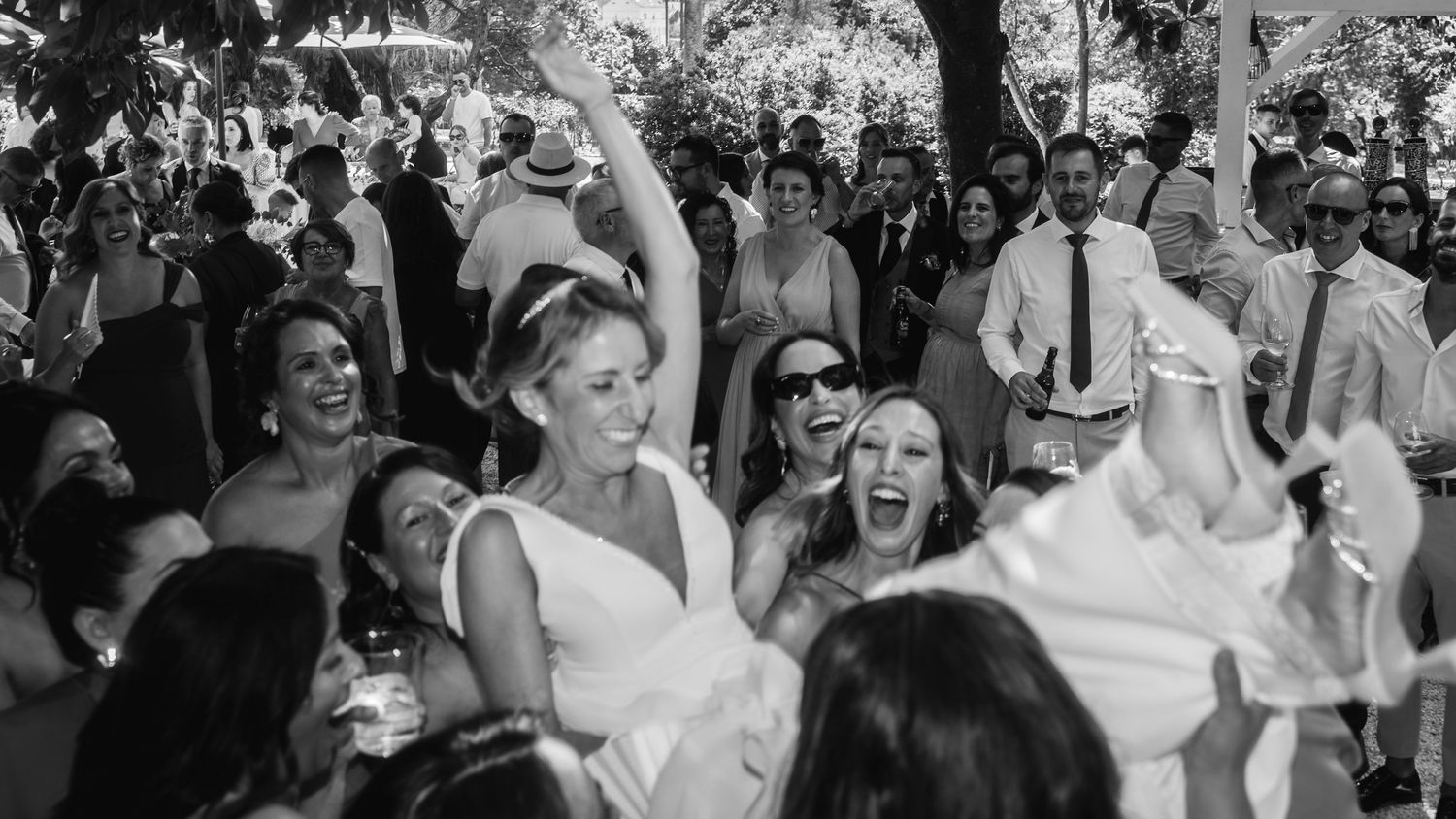 Joyful wedding celebration with guests dancing and cheering at an outdoor reception.