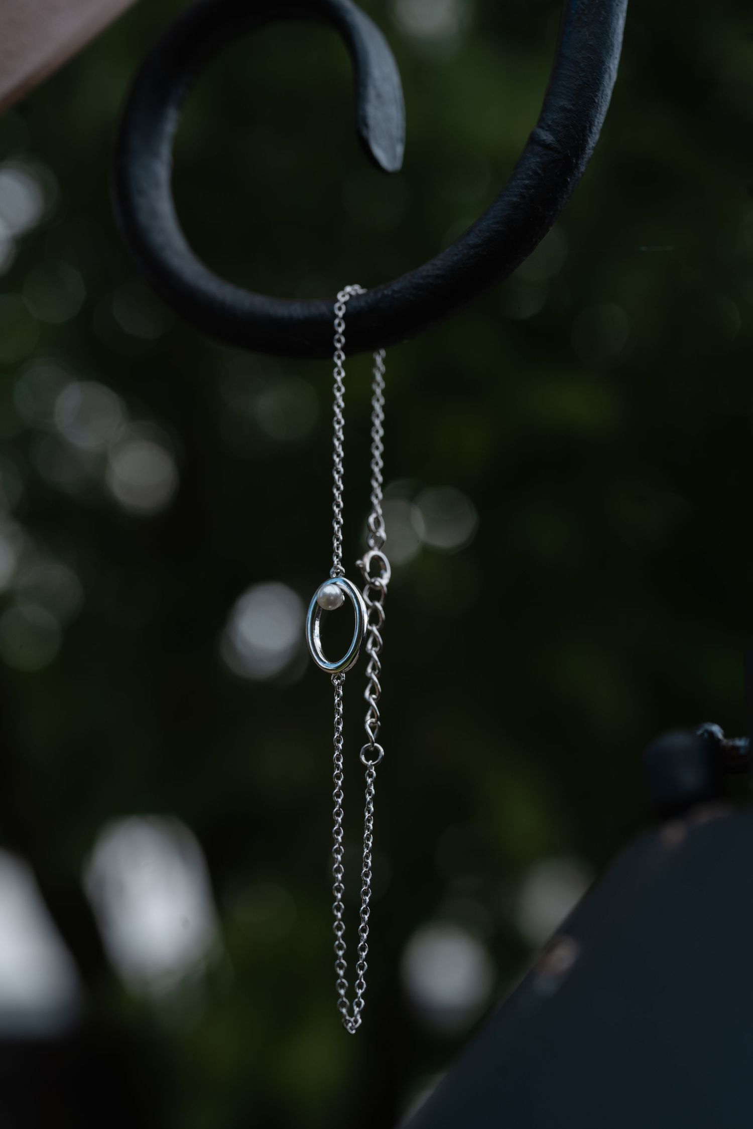 Silver chain necklace hanging against a dark blurred background with bokeh lights.