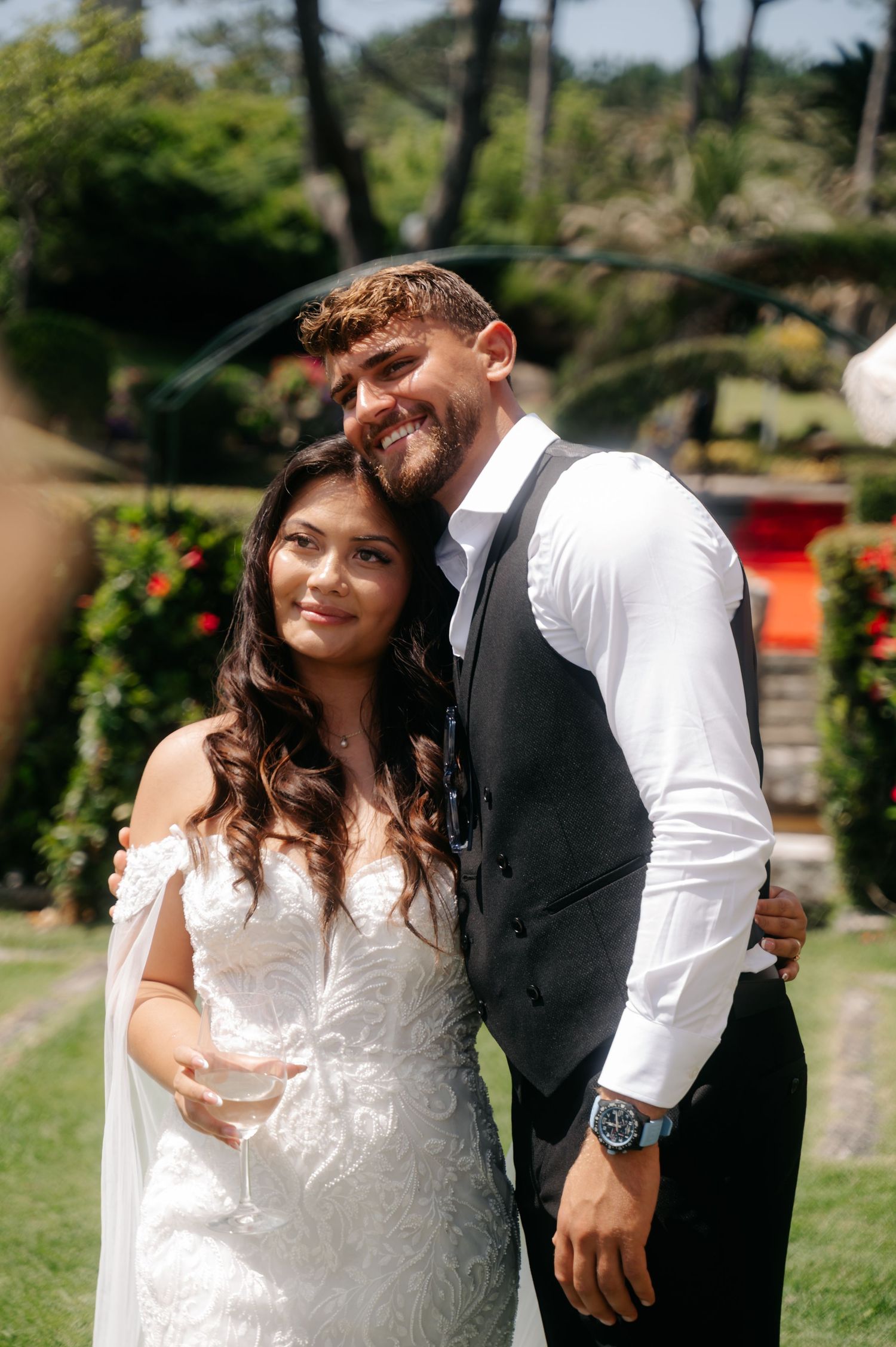 A couple in wedding attire share intimate moments in a garden setting with lush greenery and natural lighting.