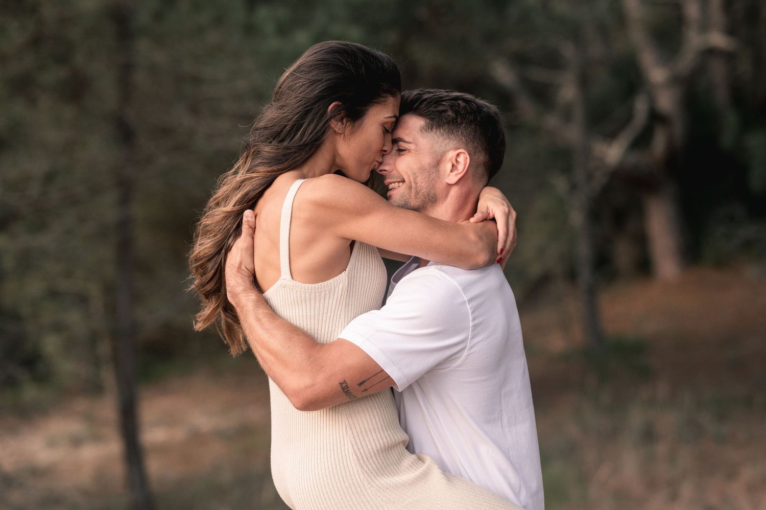A couple shares an intimate moment while standing together in a wooded area.