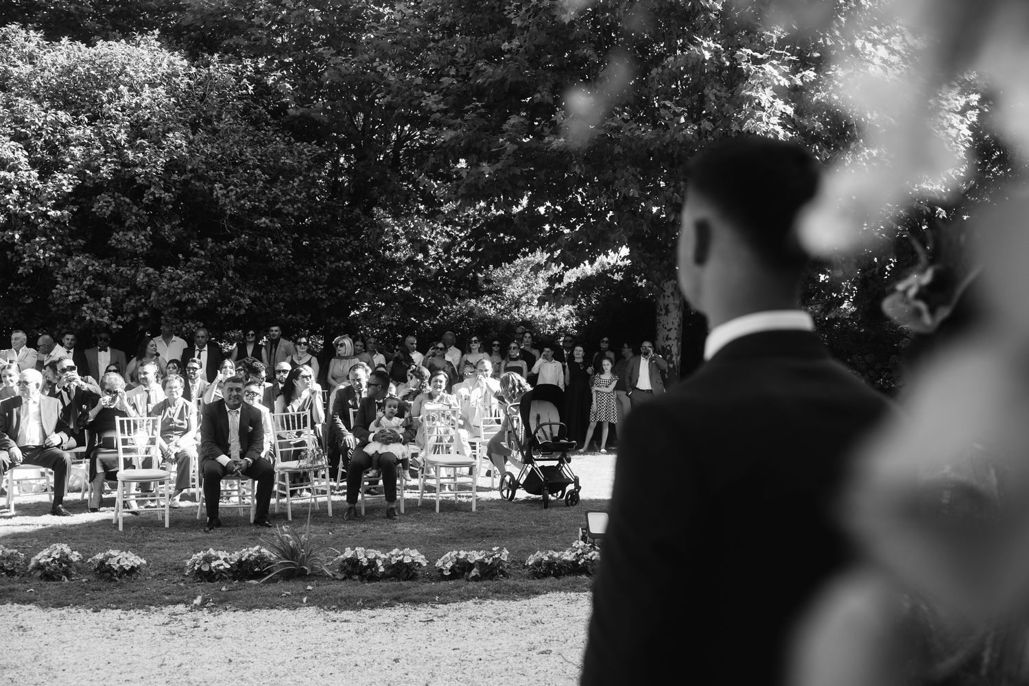 A black and white panoramic photograph of a wedding ceremony taking place outdoors under trees.