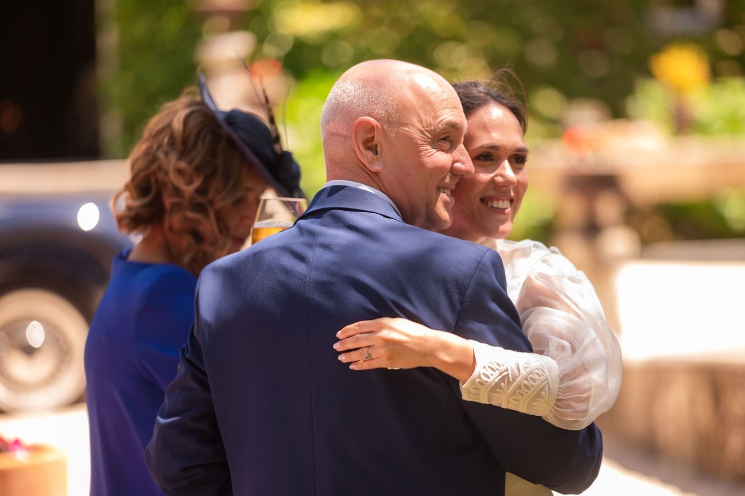 Couples dance together during a formal event in a sunlit outdoor venue.