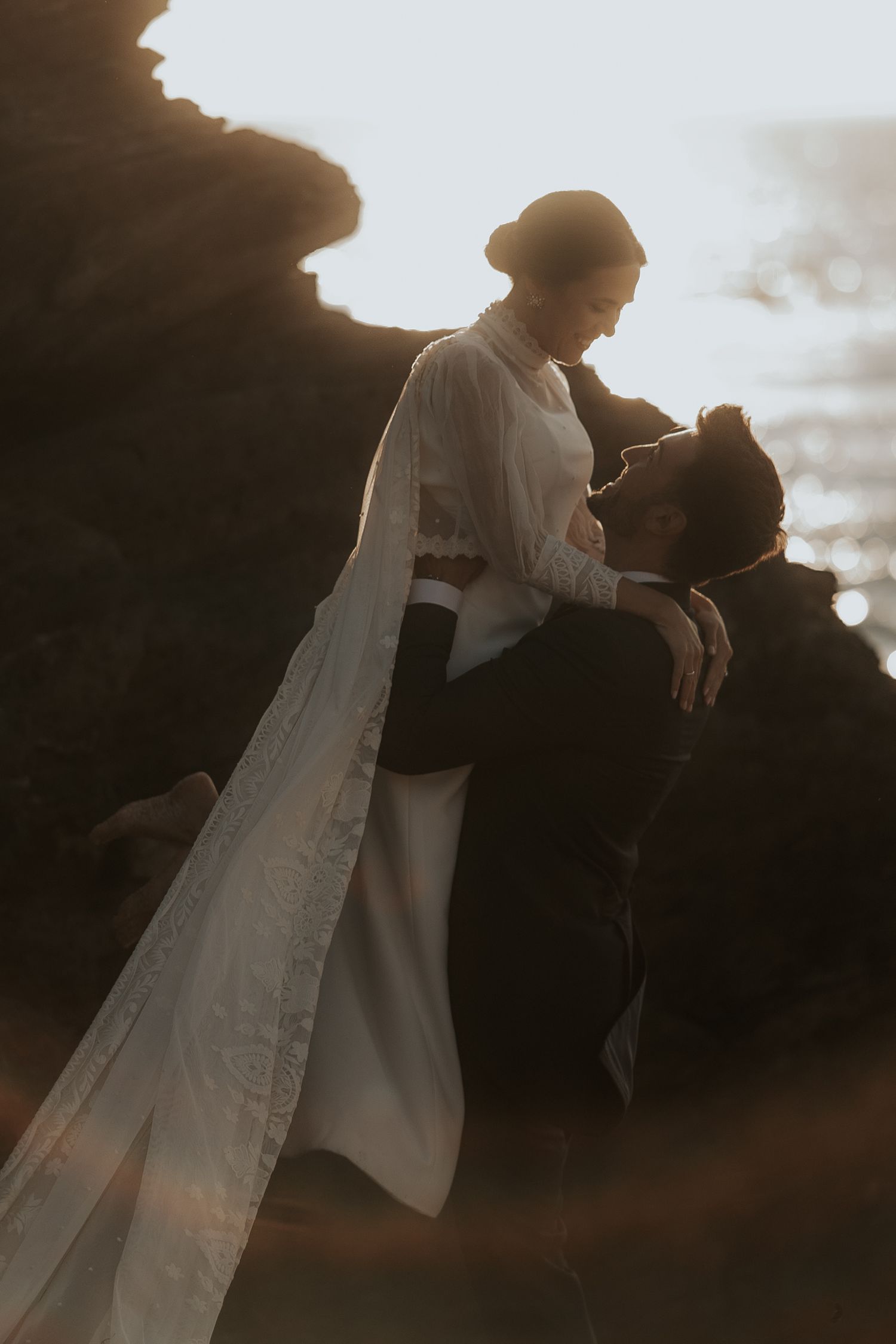Silhouettes of a couple embrace during golden hour with sunlight creating a dreamy backlit effect.