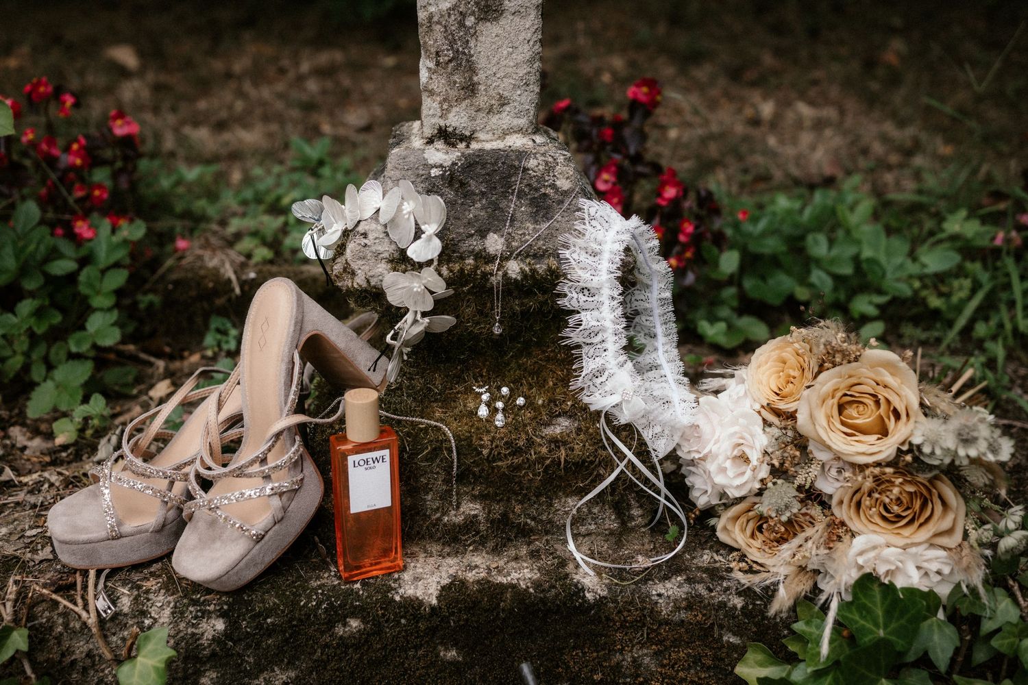 Vintage wedding details with dried roses, rings, and elegant shoes arranged on rustic white birch bark.