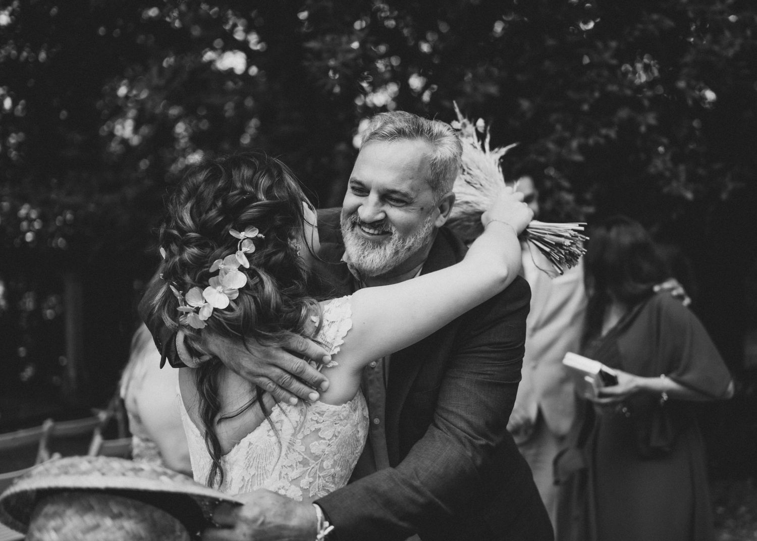 Black and white photo of joyful wedding embrace outdoors with trees in background.