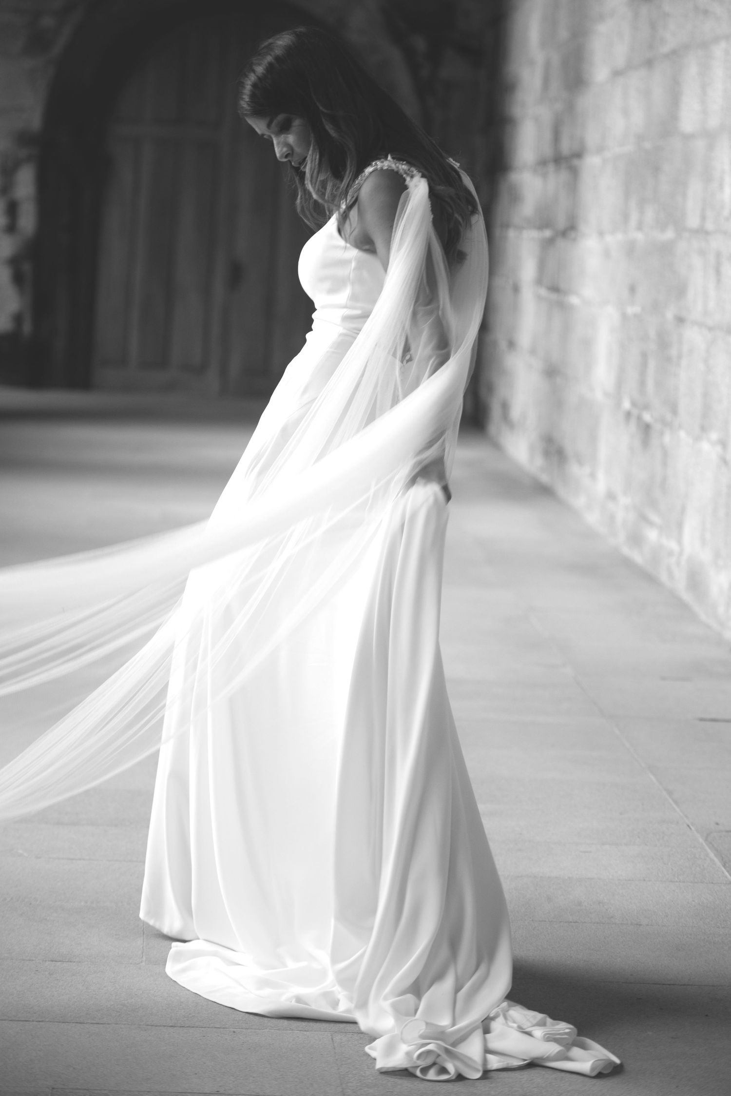 Flowing white wedding dress billows elegantly against stone wall backdrop.