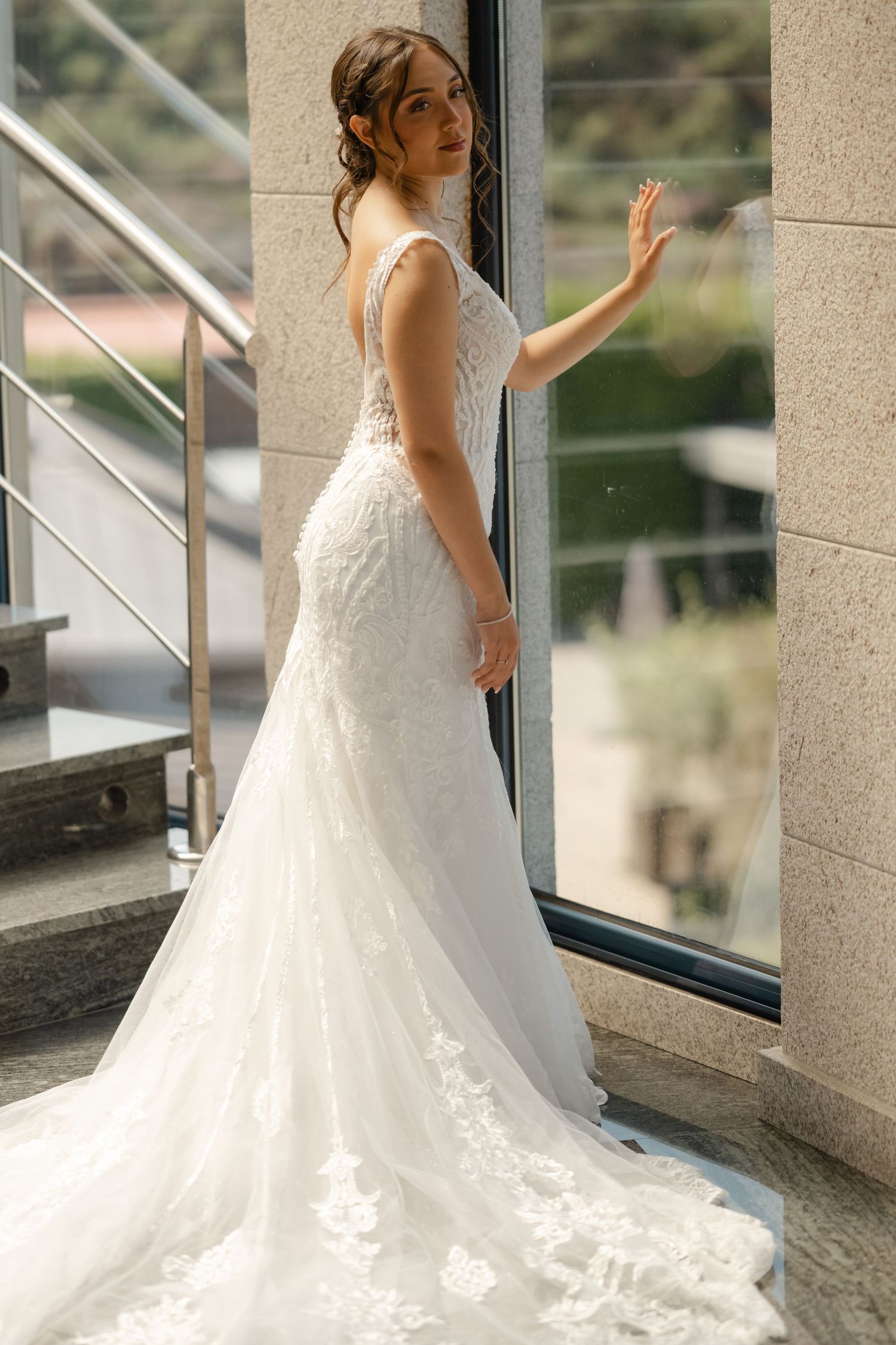 Wedding dress with intricate lace detail and flowing train photographed near large windows.