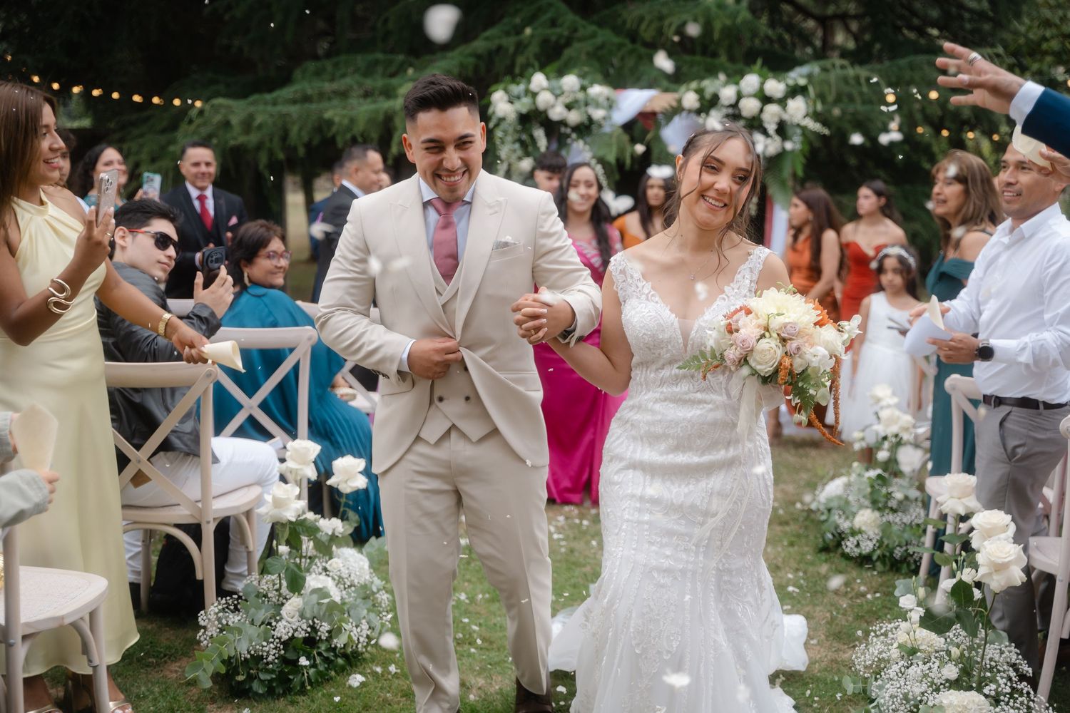 Wedding guests throw flower petals at a joyful couple during an outdoor garden celebration.