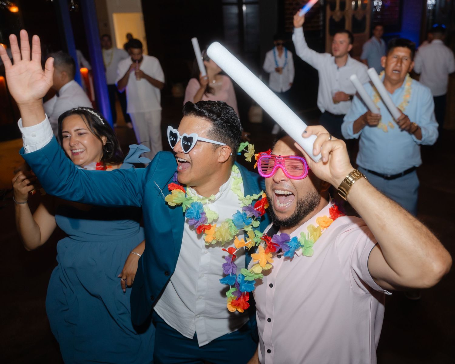 Party guests dancing with colorful Hawaiian leis and sunglasses at a nighttime celebration.