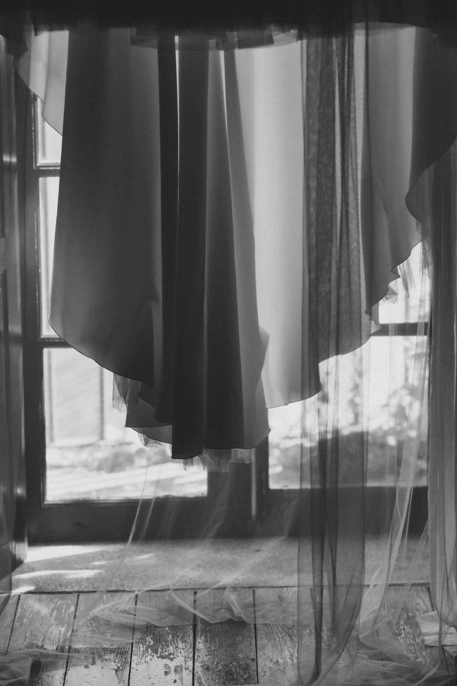 Black and white image of hanging garments creating dramatic shadows and silhouettes against a bright window.