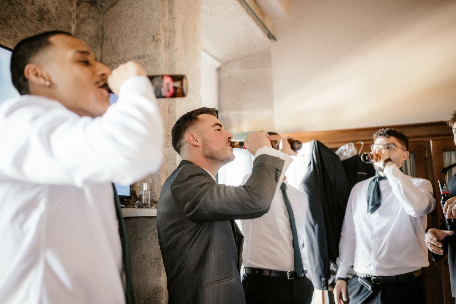 A group of groomsmen in formal attire take celebratory shots together at a wedding reception.