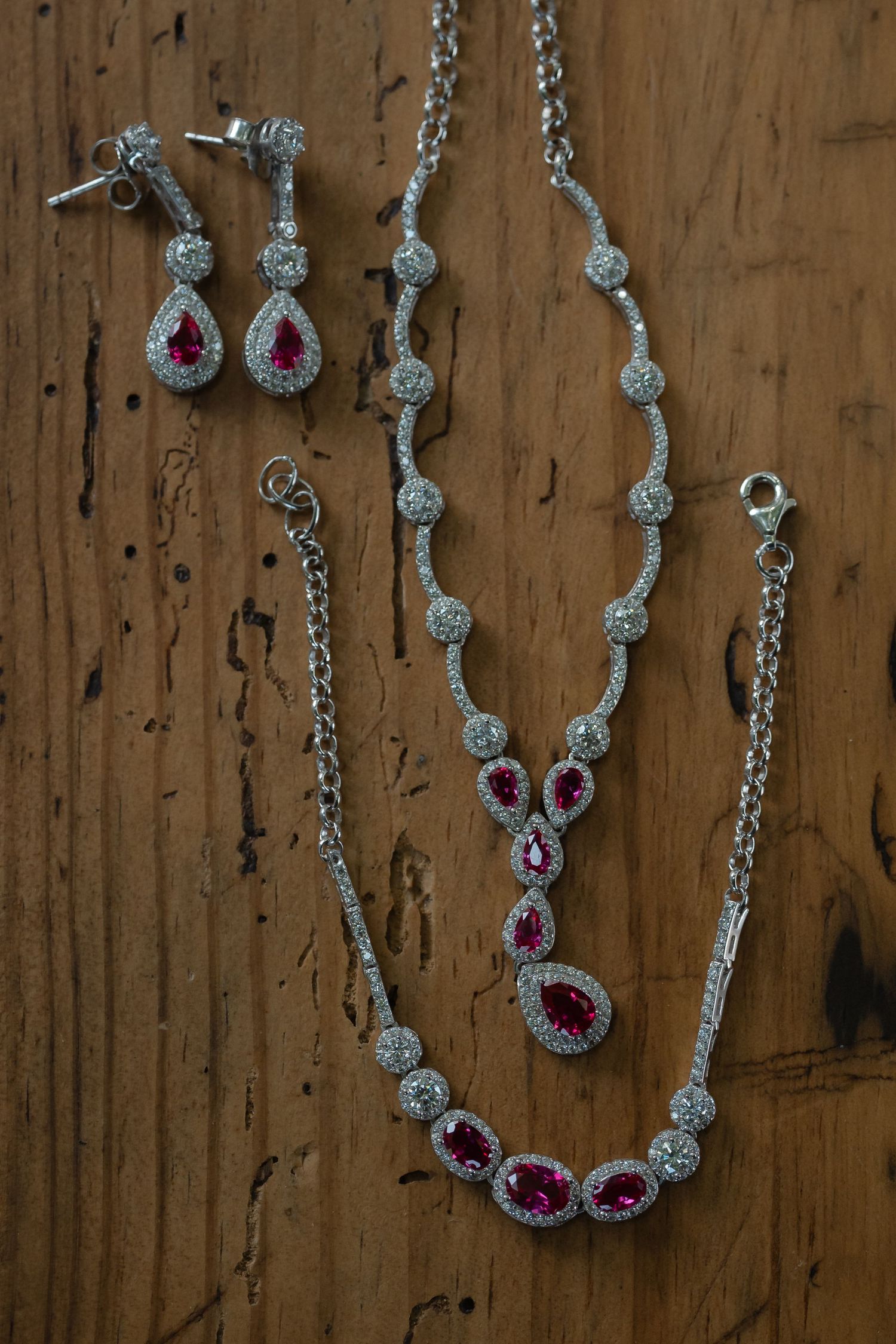 Elegant silver jewelry set featuring pink gemstones and crystal accents displayed on rustic wooden background.