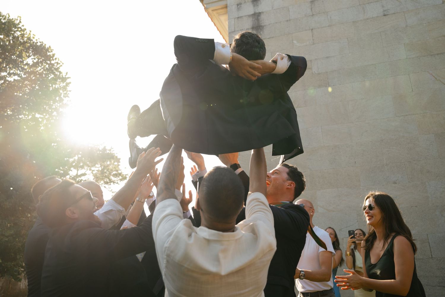 A celebratory moment as wedding guests lift someone up during an outdoor reception.
