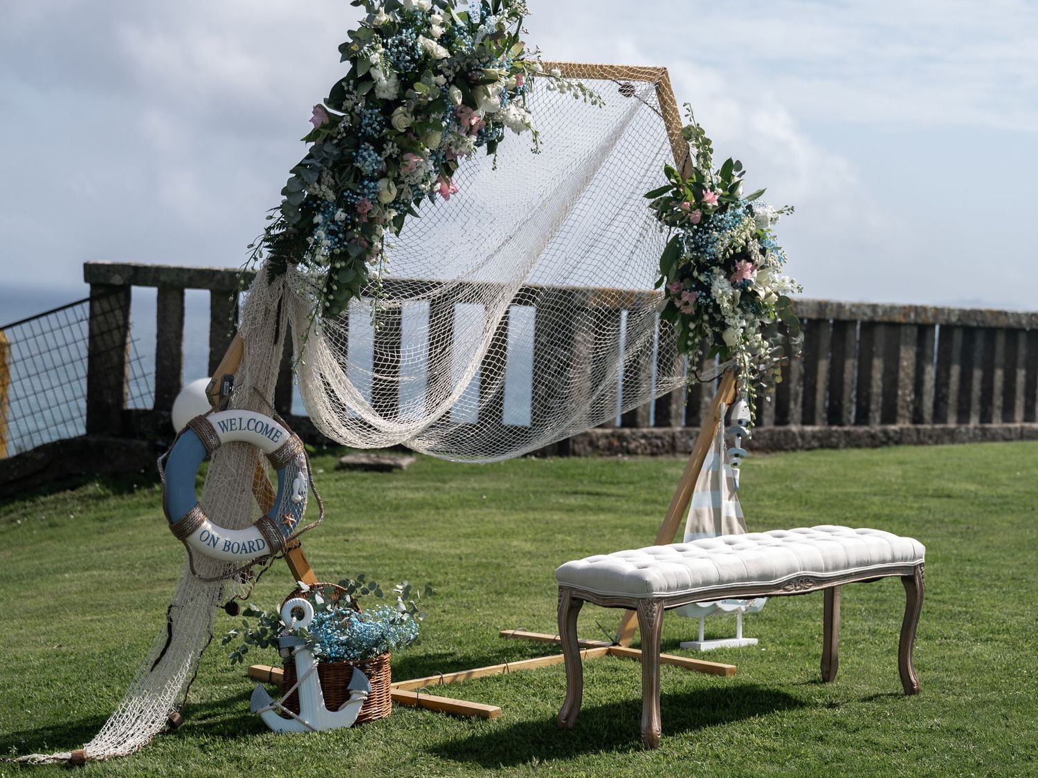 Outdoor wedding ceremony setup with white fabric arch, wooden benches, and floral decorations on a grassy lawn.