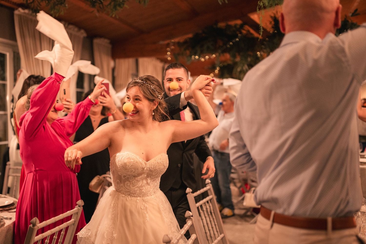 Wedding guests dance together during an evening reception celebration under outdoor lighting.