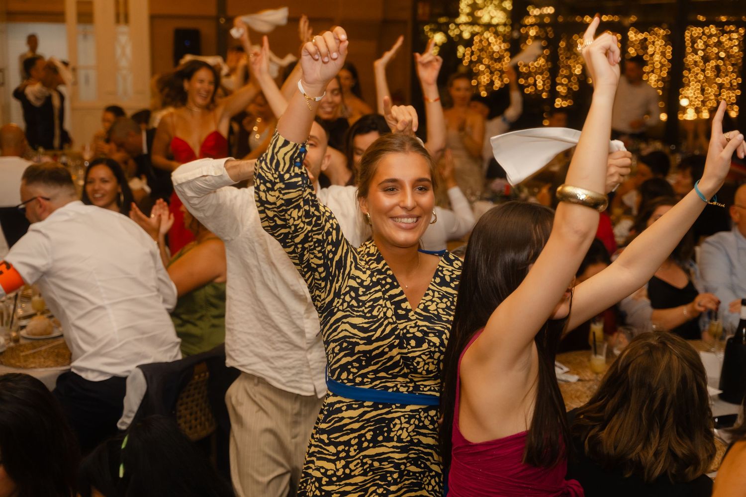 Energetic crowd dancing and celebrating at a festive indoor party with warm lighting and holiday decorations.