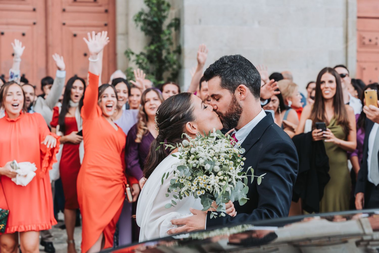 Wedding guests in coral dresses gather outside a venue during a celebration.