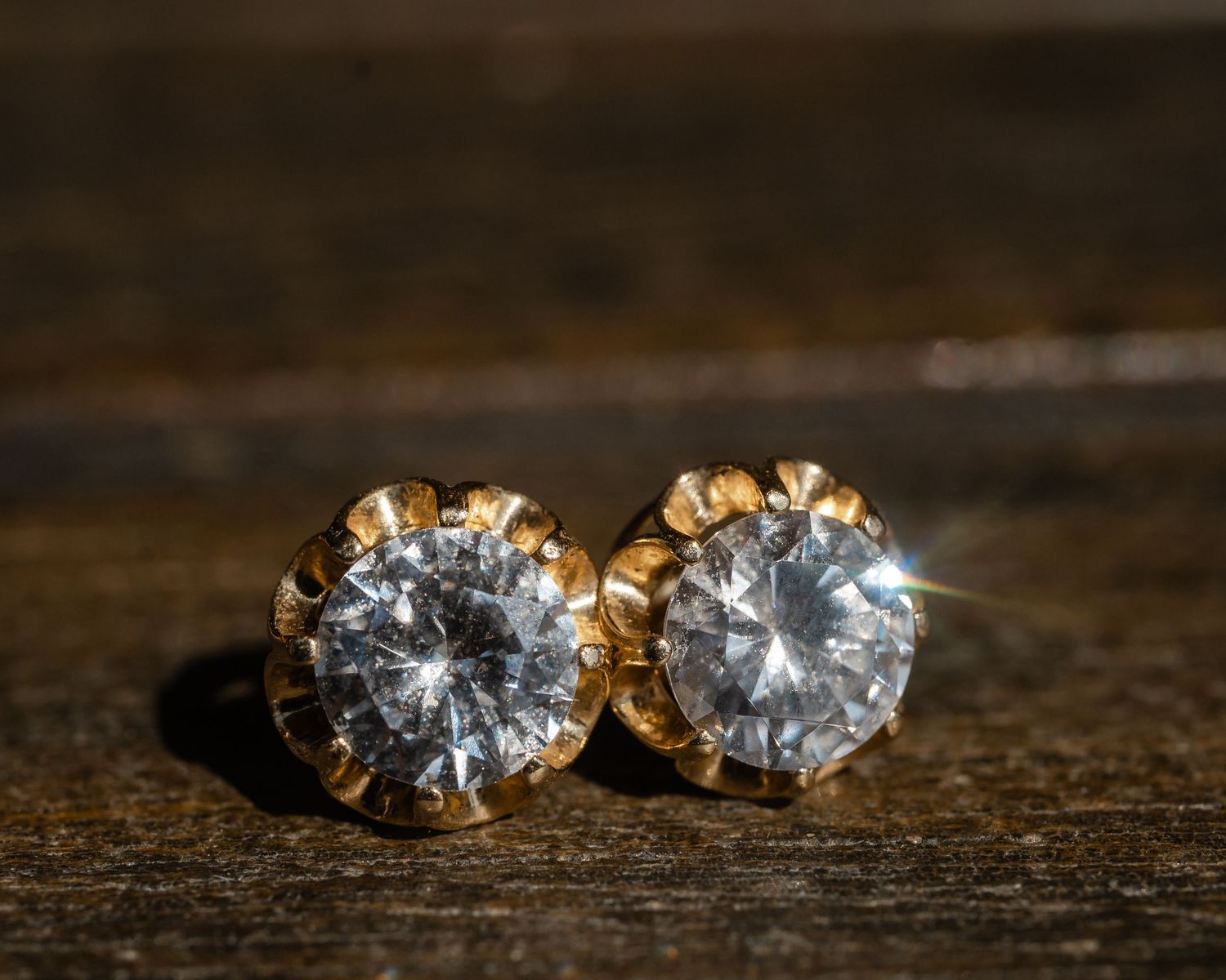 Close-up view of diamond stud earrings with gold settings on a dark wooden surface.