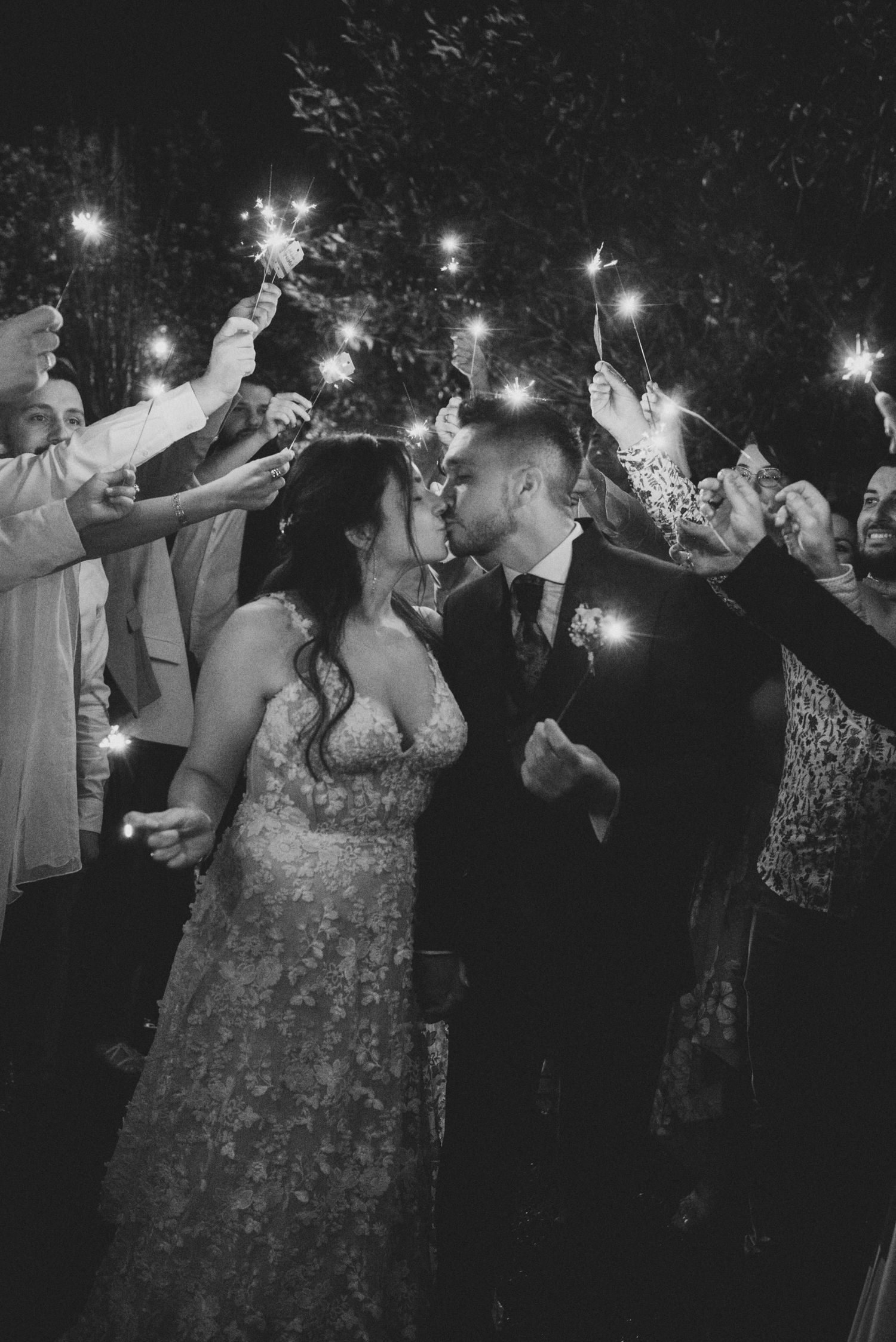 Wedding guests hold sparklers in the dark during an outdoor nighttime celebration sequence.