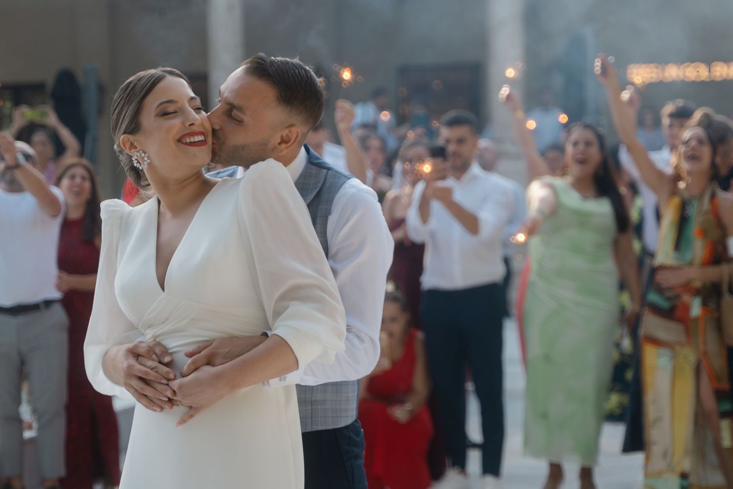 A couple dancing together at a wedding reception while guests look on and applaud in the background.