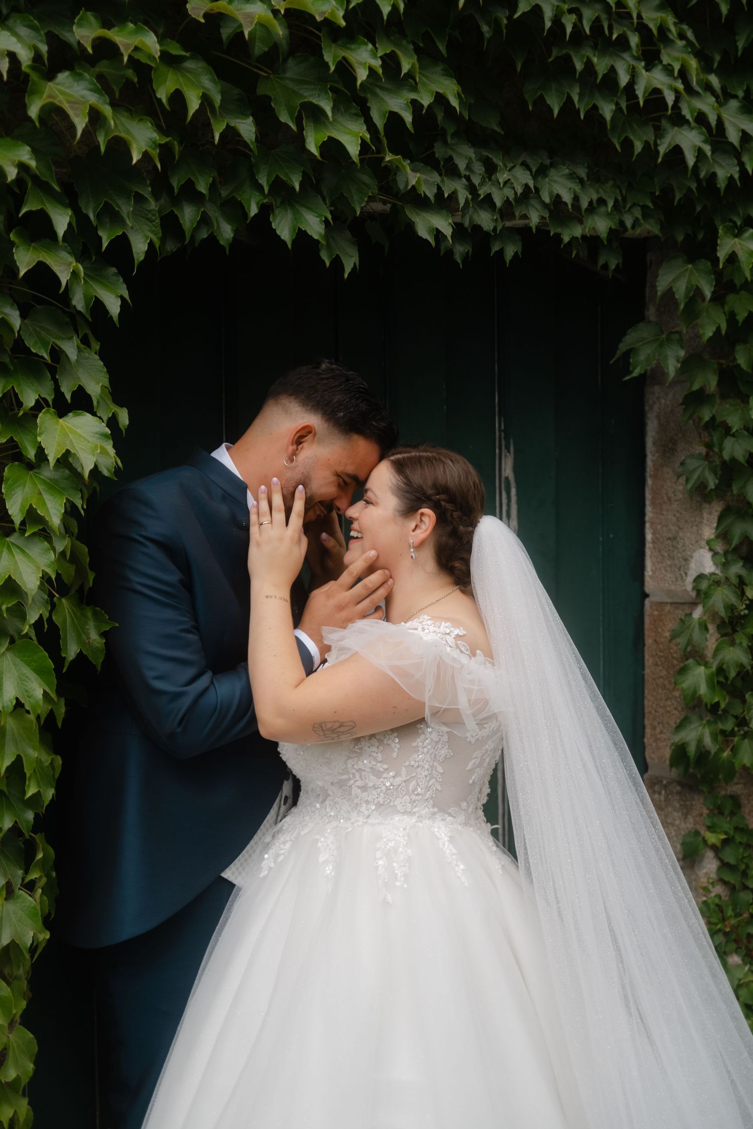 A romantic wedding moment captured against a backdrop of lush green ivy vines on a wall.