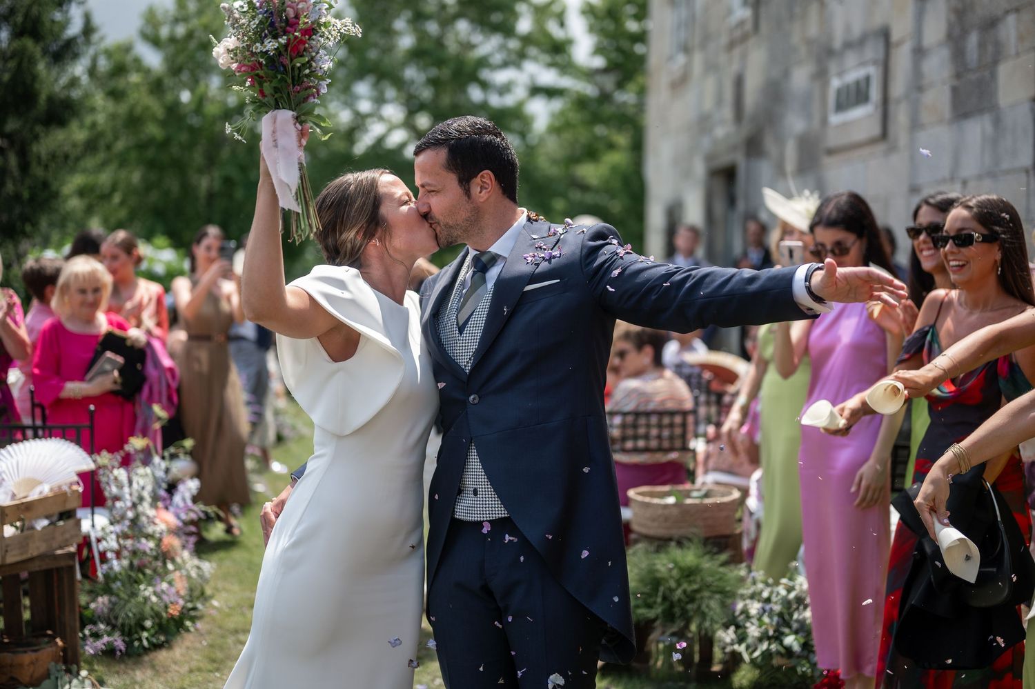 Wedding celebration in a garden setting with guests gathered around the newlyweds.